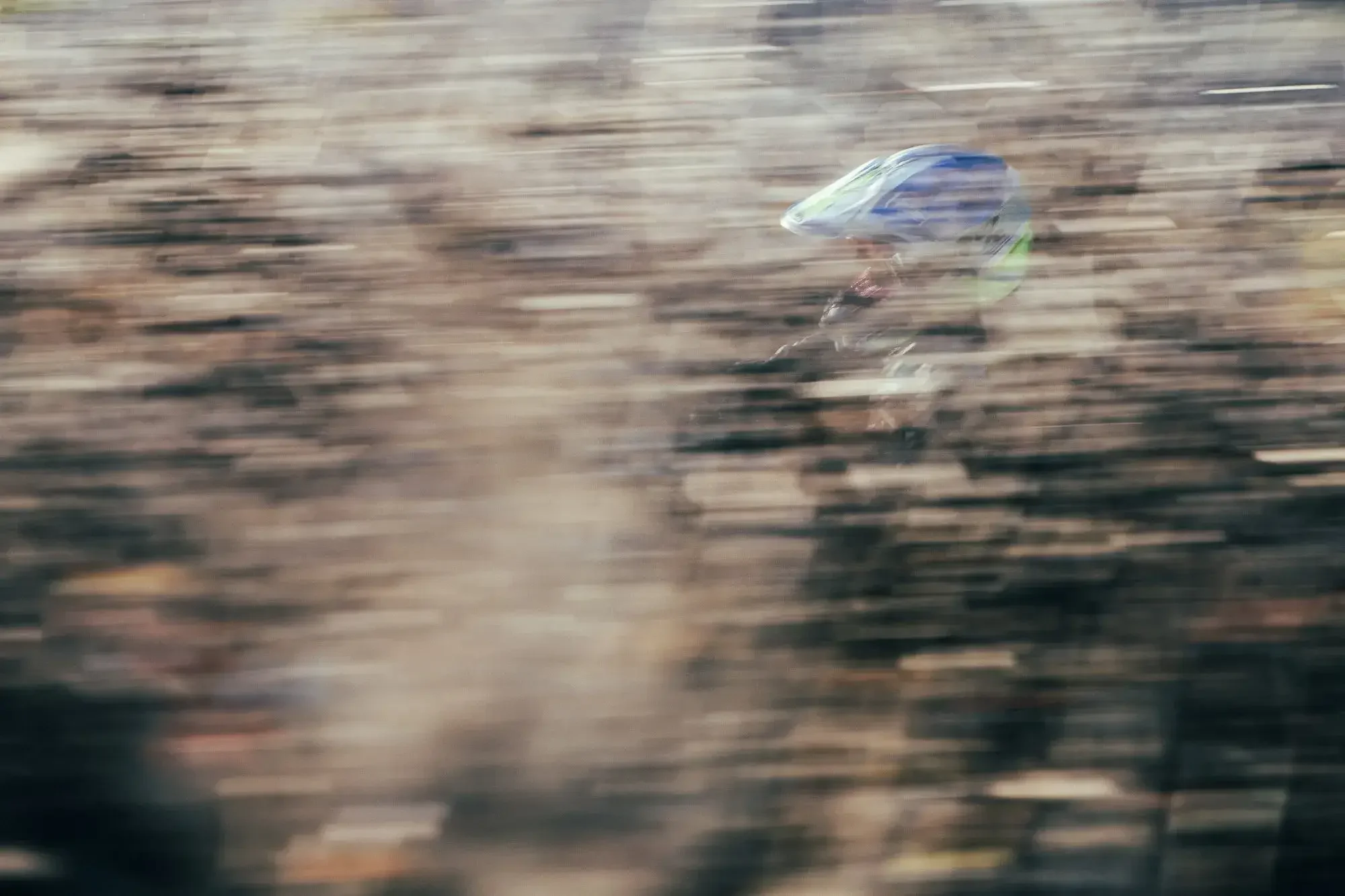 A person riding a motorcycle wearing a helmet, captured in motion with a blurred background.
