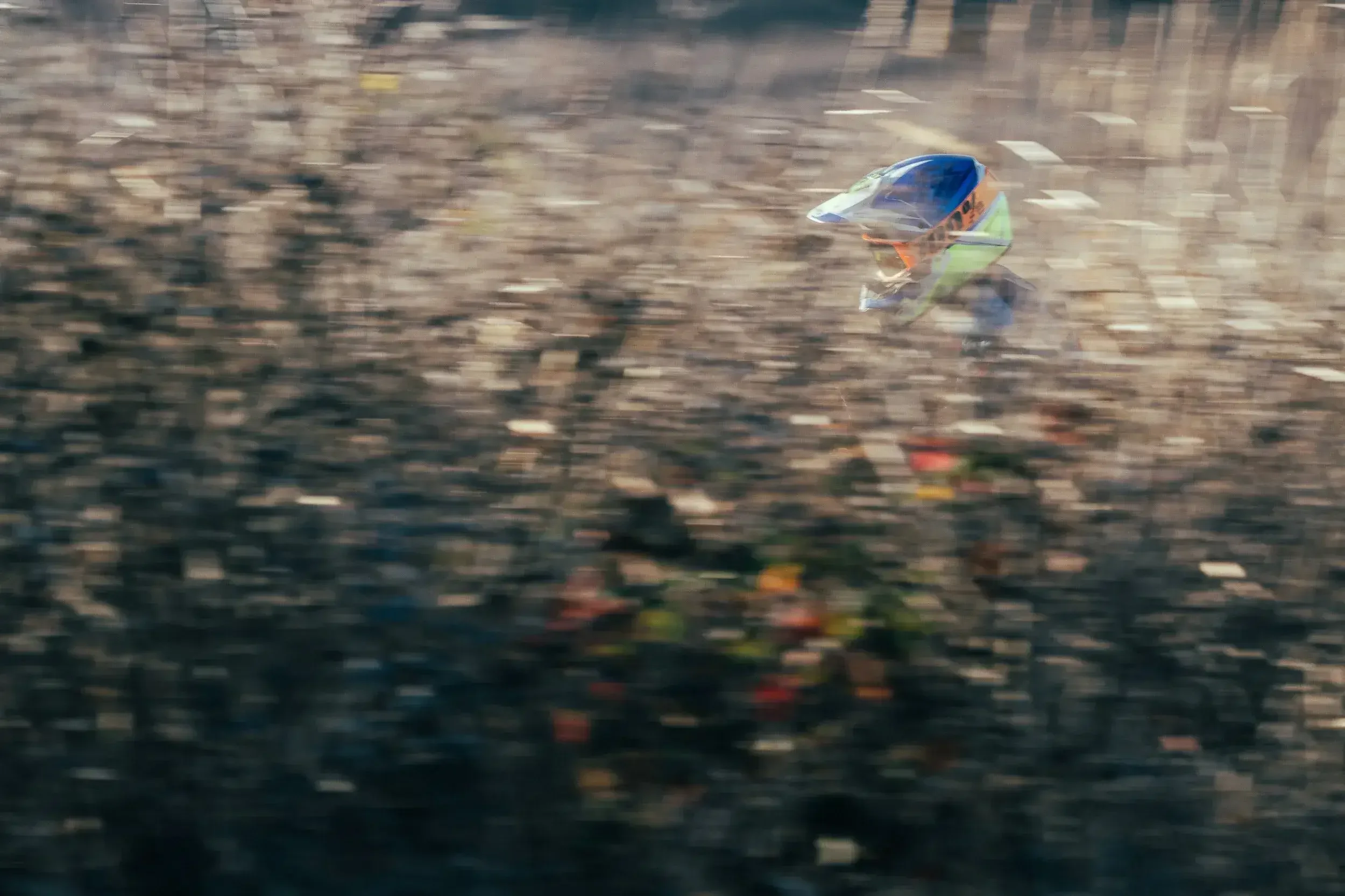 A person wearing a helmet and reflective vest riding a dirt bike through a blurred forest trail.
