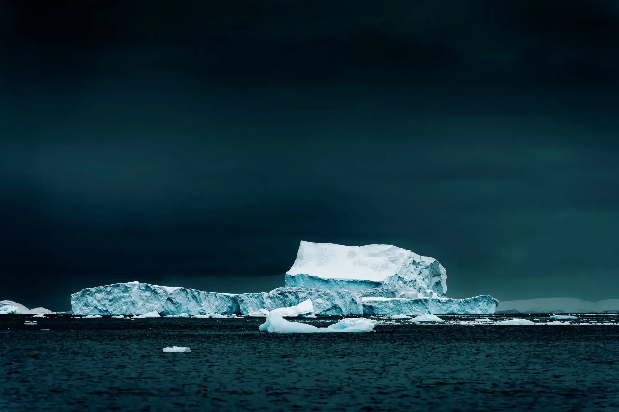 A large iceberg floating in dark ocean water under a cloudy sky.