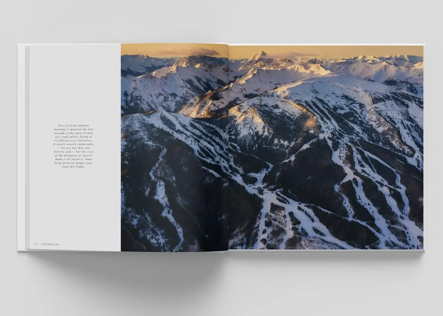 Open book displaying a two-page spread of a photograph showing snow-covered mountain range at sunset with some sparse trees on the slopes.