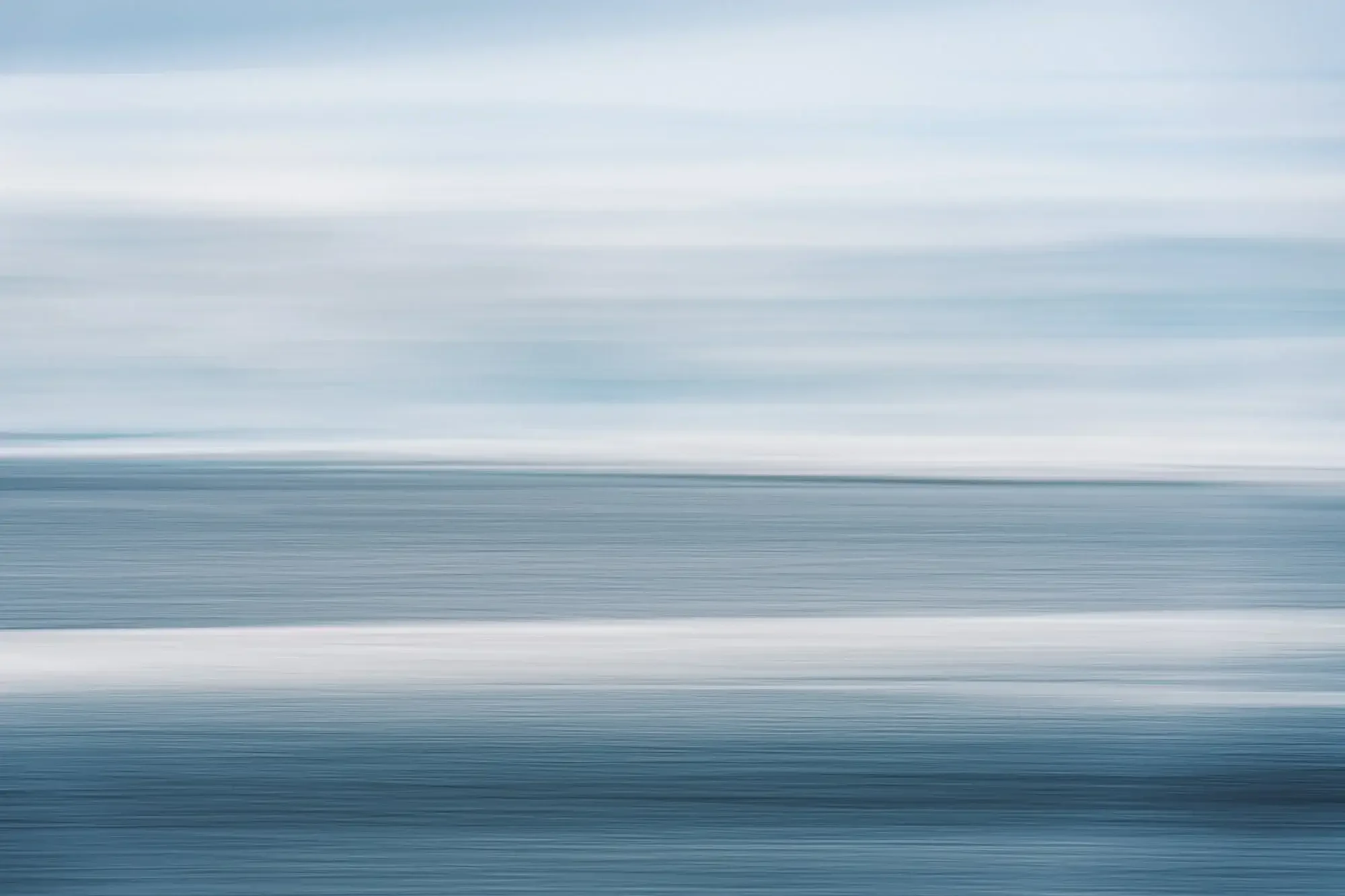 Abstract image with horizontal streaks of blue, white, and gray resembling a blurred seascape or sky.