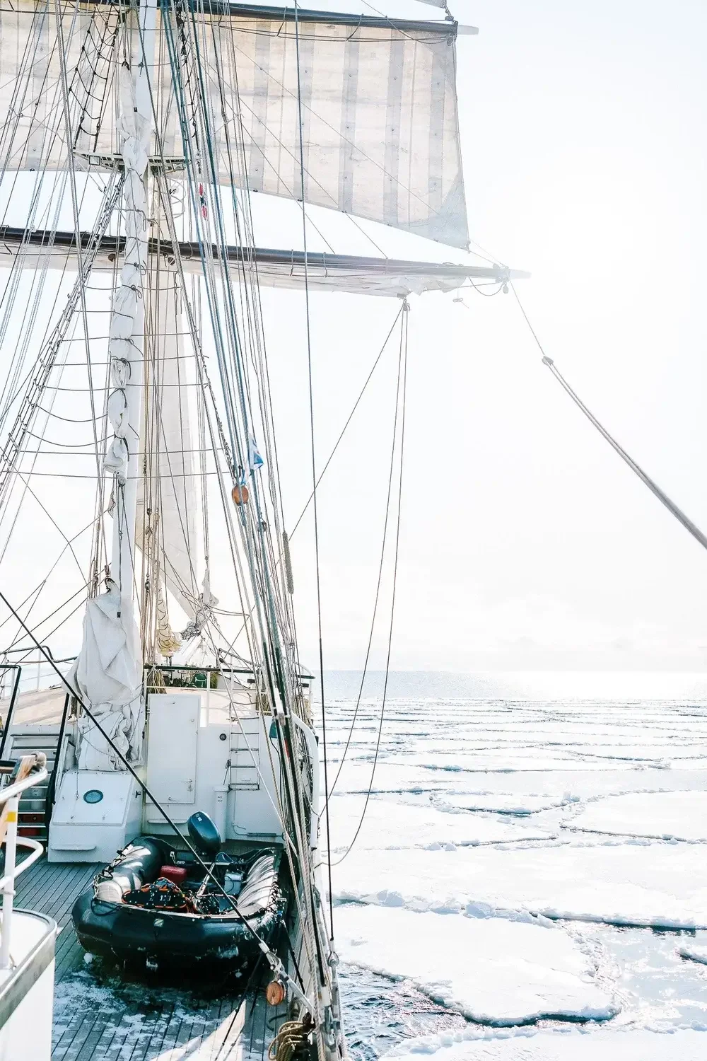 A sailing ship on icy water, with snow and ice-covered surface under bright, overcast sky.
