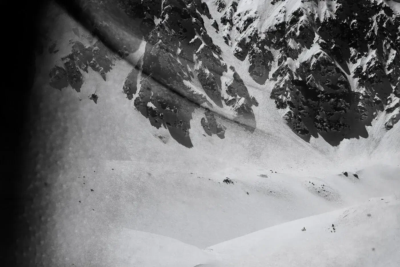 Black and white photo of a snowy mountain landscape with trees, snowy slopes, and shadows.