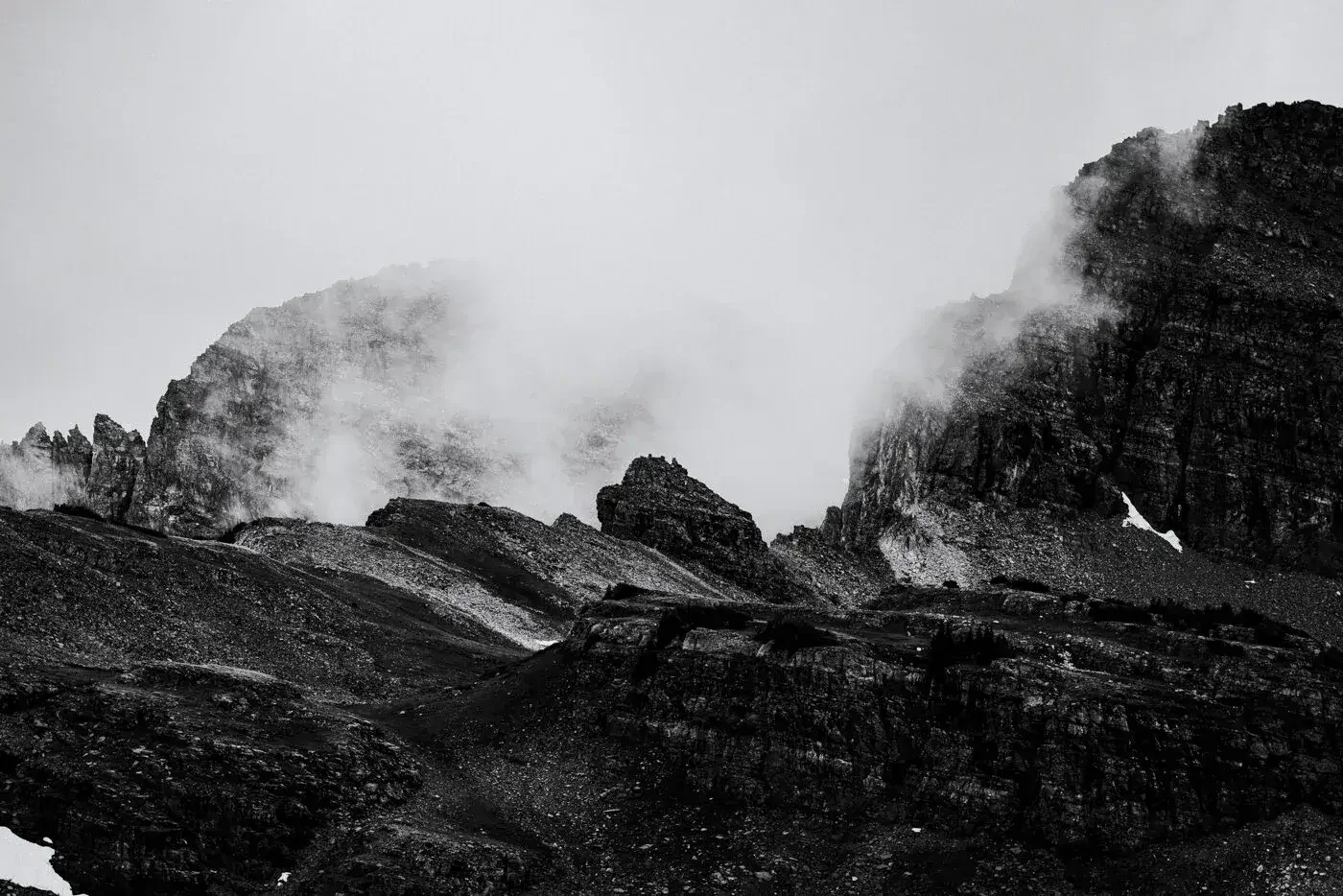 Black and white photograph of rugged mountain peaks with mist and clouds around the summits.