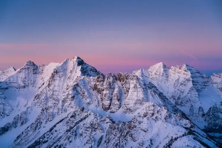 Snow-covered mountain range under a colorful sky at sunrise or sunset.
