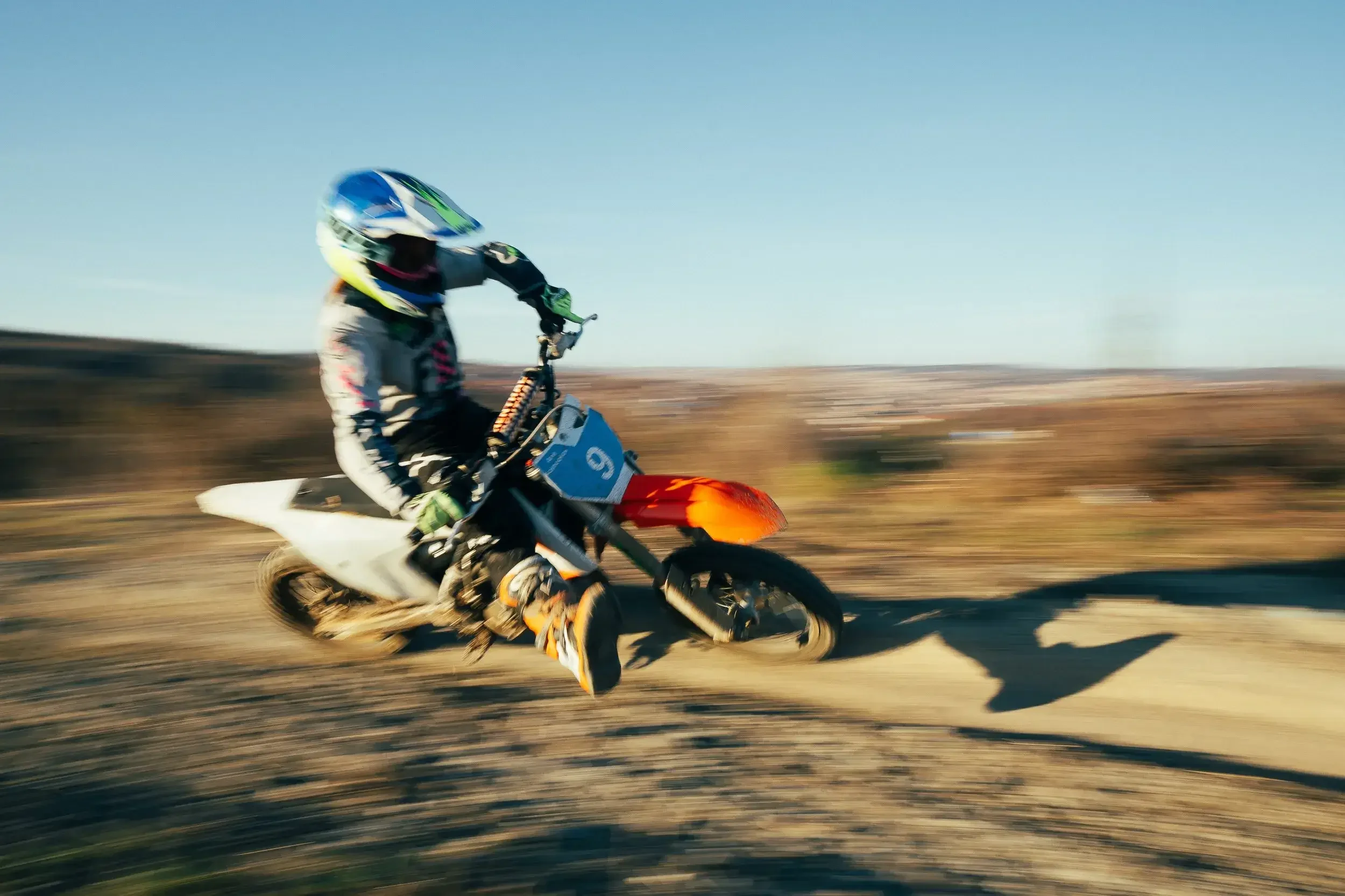 Motocross rider wearing a helmet and protective gear riding on a dirt track, with motion blur indicating high speed.
