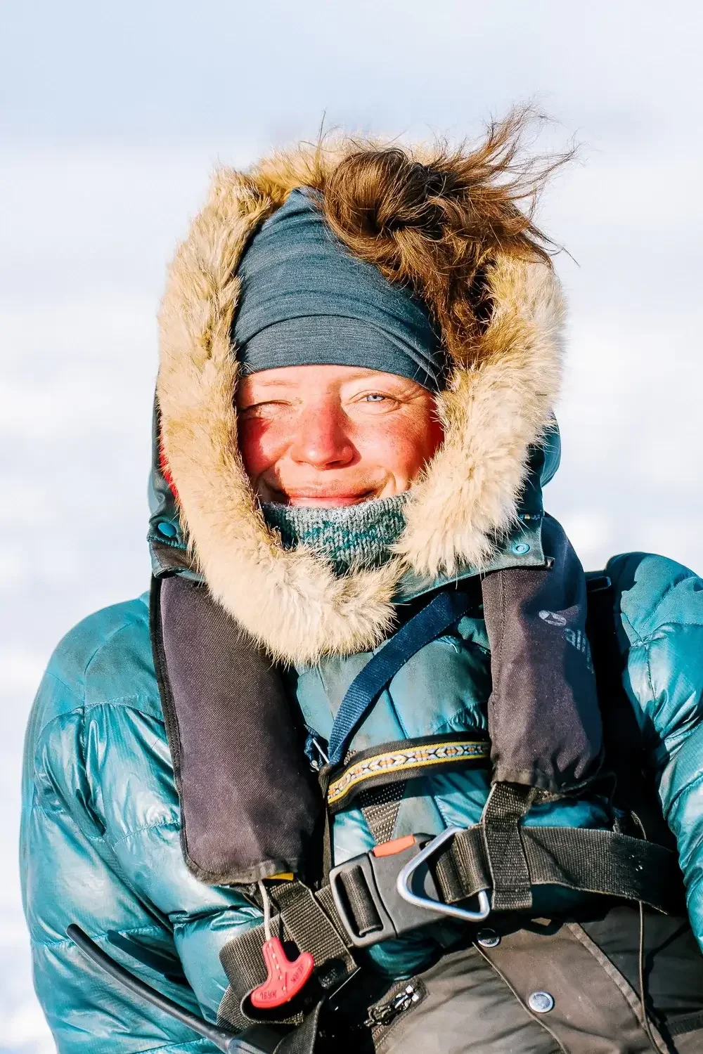 Woman dressed in winter gear, smiling with one eye closed, outdoors in cold weather.