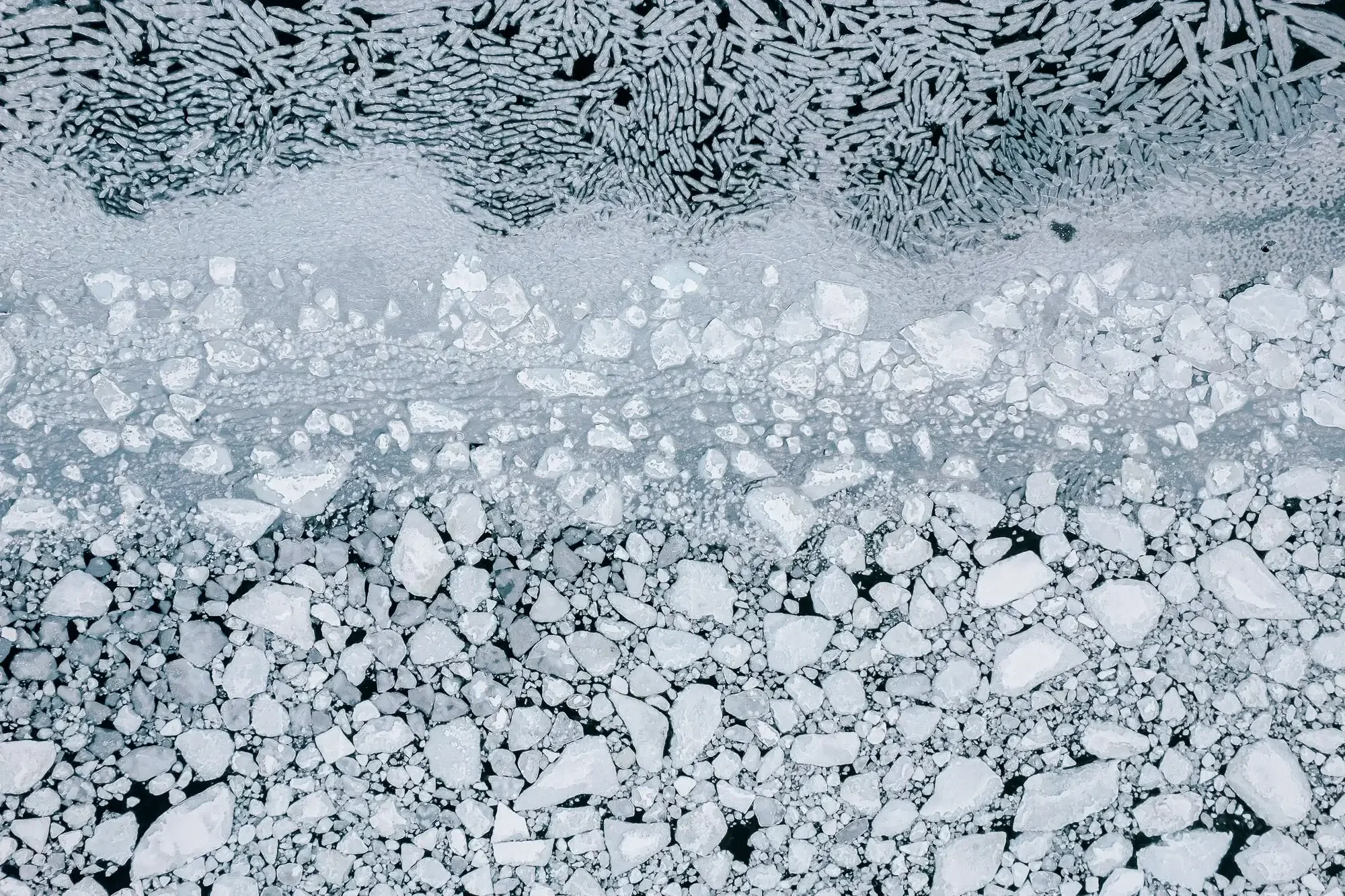 Aerial view of a frozen river with cracked ice and rocky shoreline