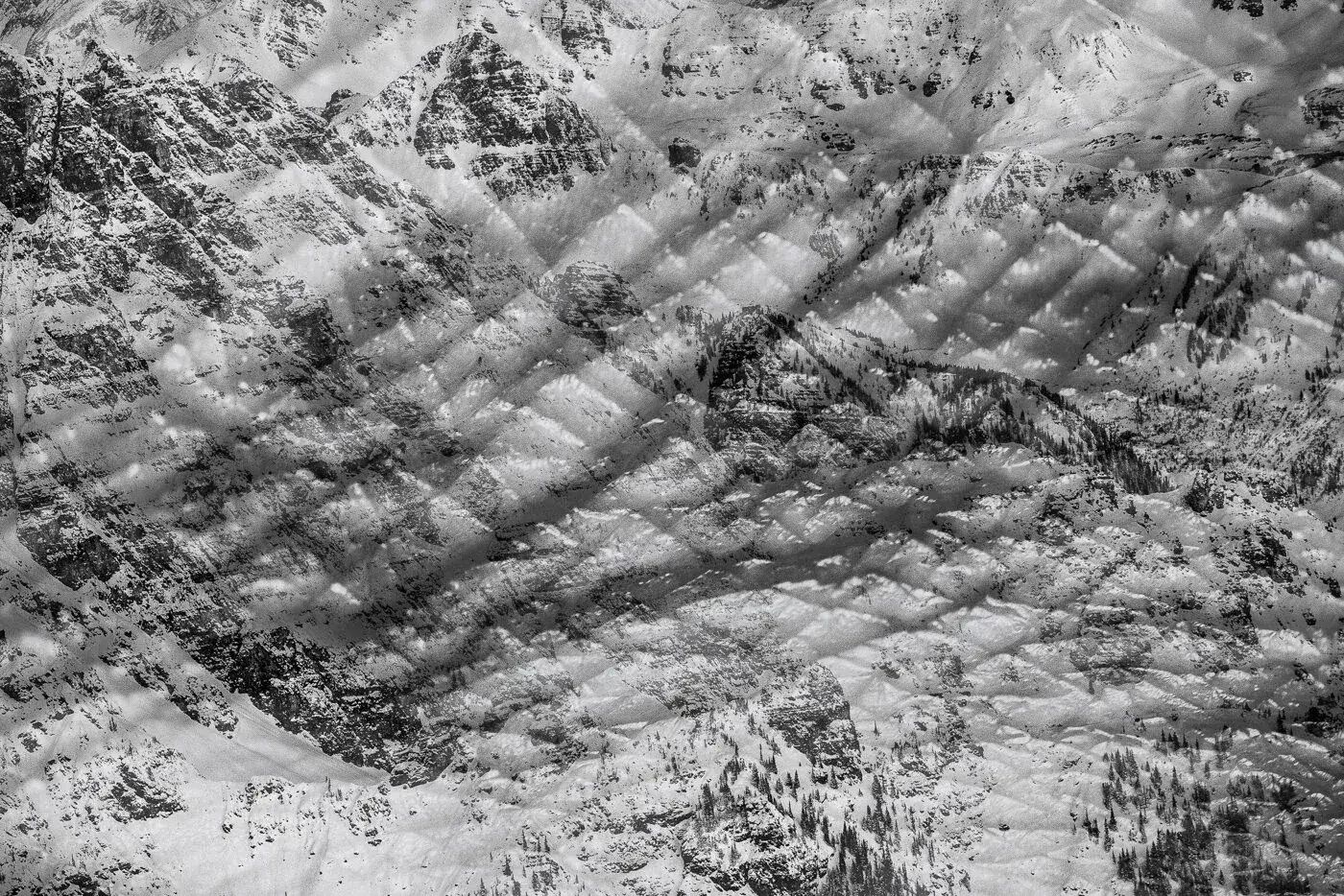 Snow-covered mountain range with rugged peaks and trees in a monochrome color scheme.
