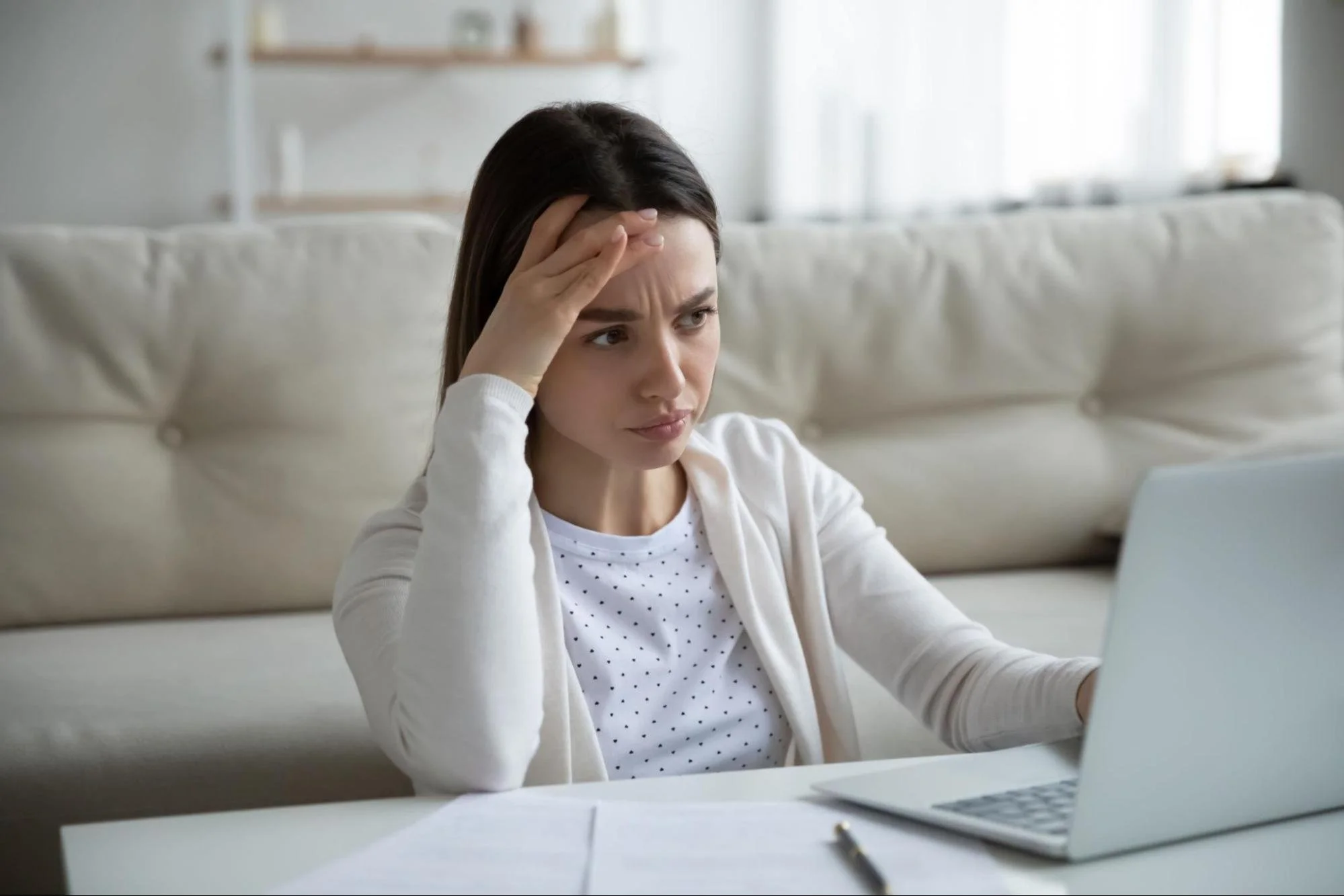 A troubled woman looking at her laptop in her home.