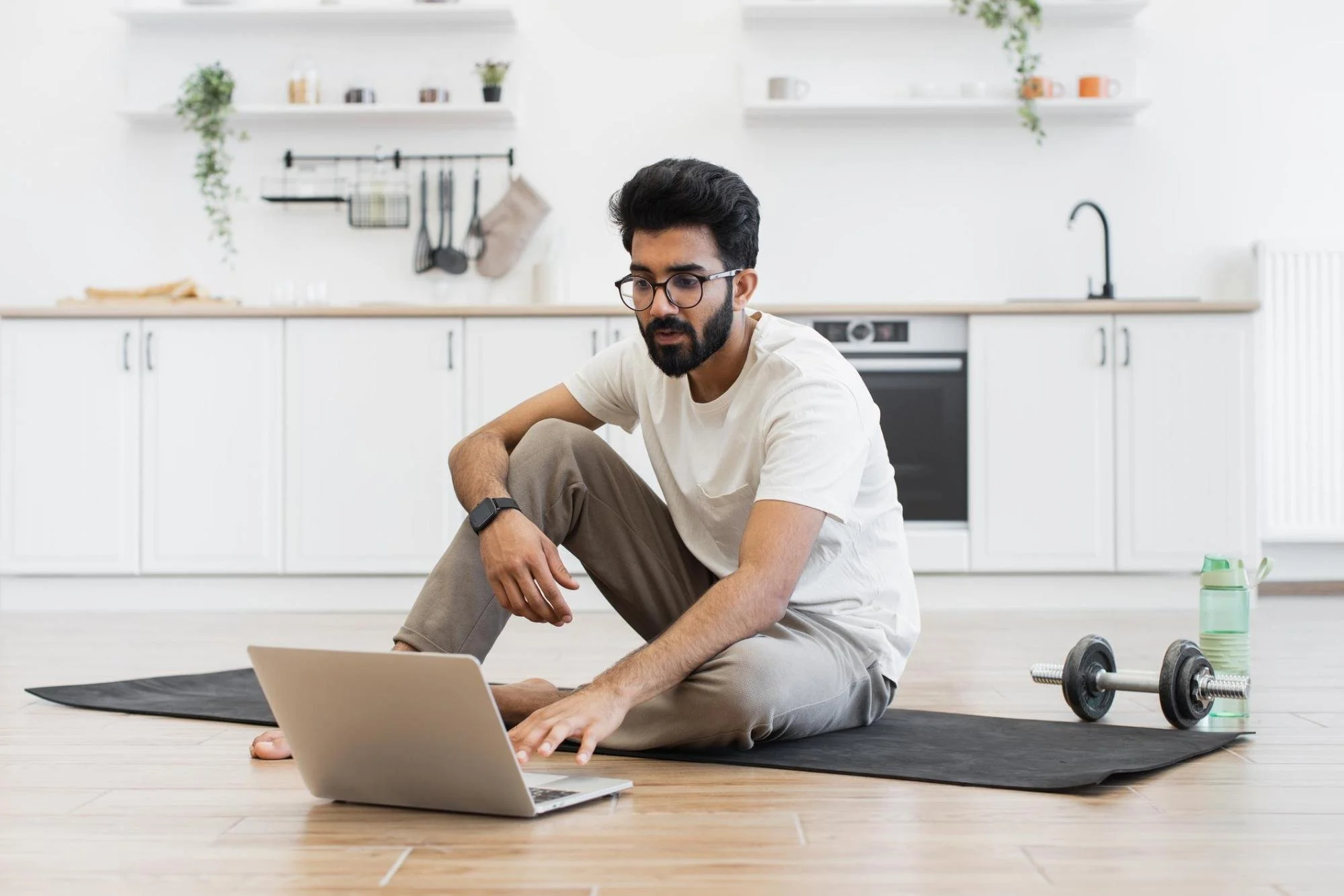 A guy using his laptop while sitting on a yoga mat.