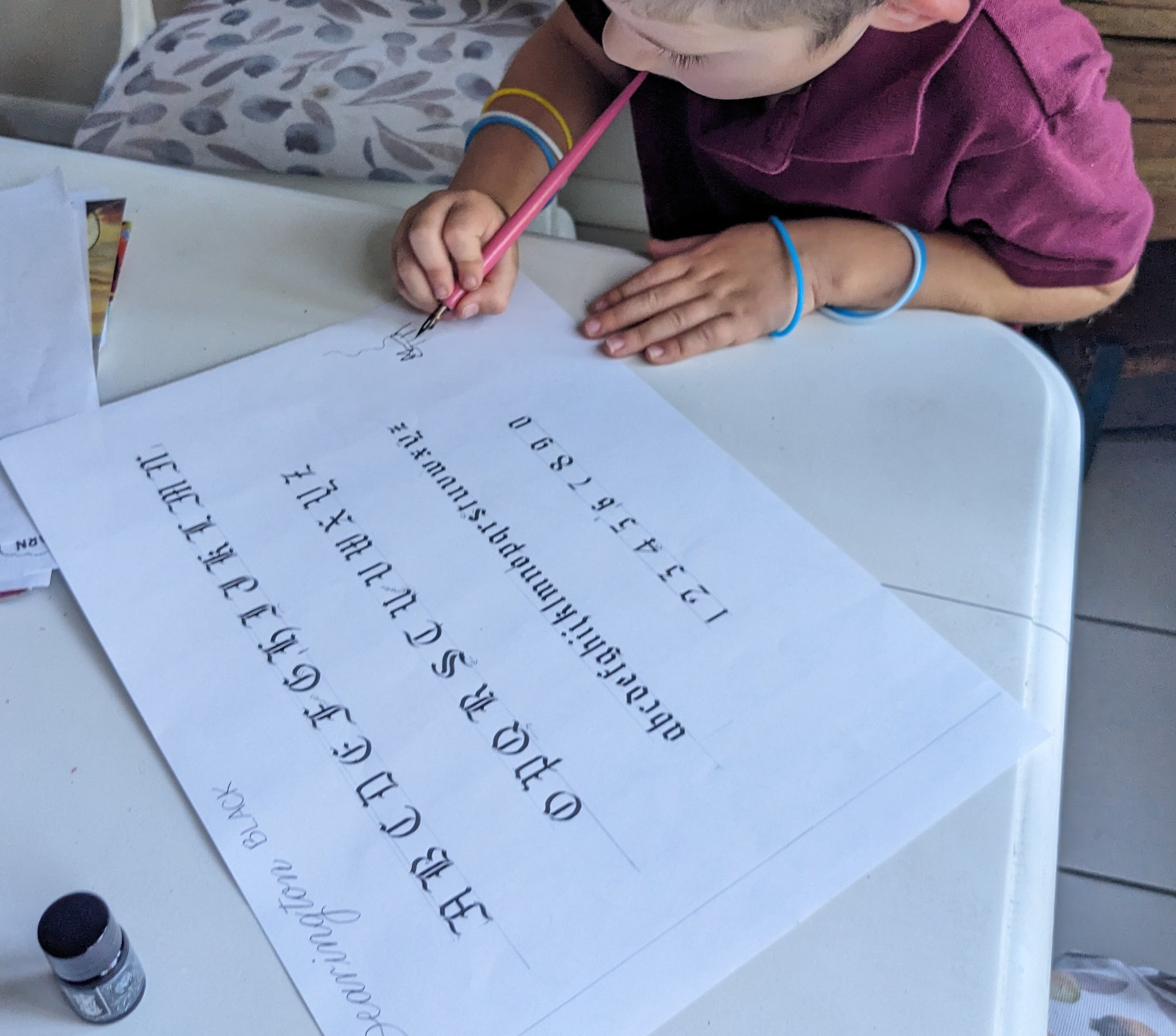 young boy draws with a dip pen and ink