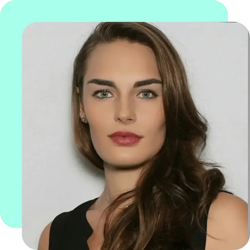 A woman with long, wavy brown hair, light skin, green eyes, wearing makeup and a sleeveless black top, standing against a plain white background.