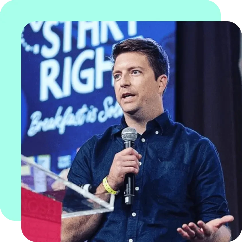 Man speaking into a microphone at an event with a backdrop that reads 'Start Right' in bold letters.