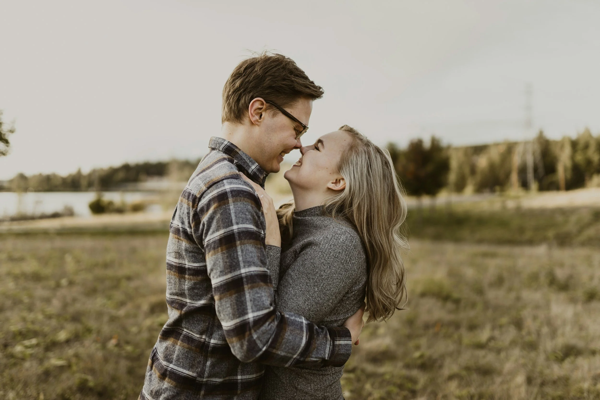 A couple laughing together, foreheads touching, in an open field