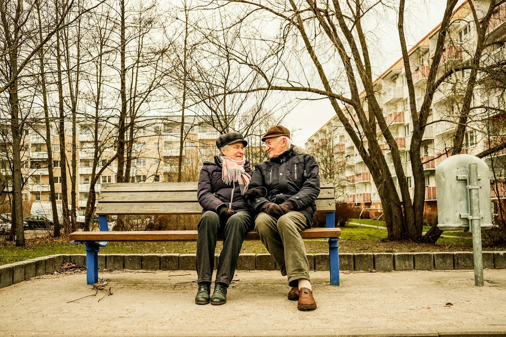 An older couple on a park bench, turned toward each other