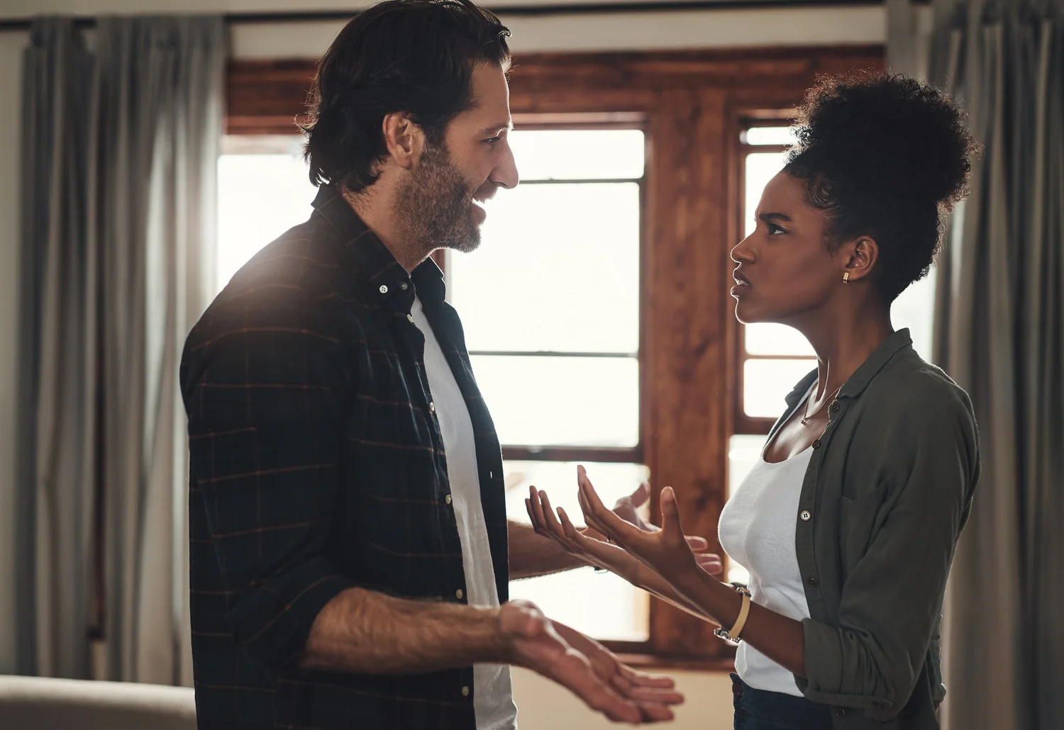 A couple standing in their living room mid-conversation, turned toward each other
