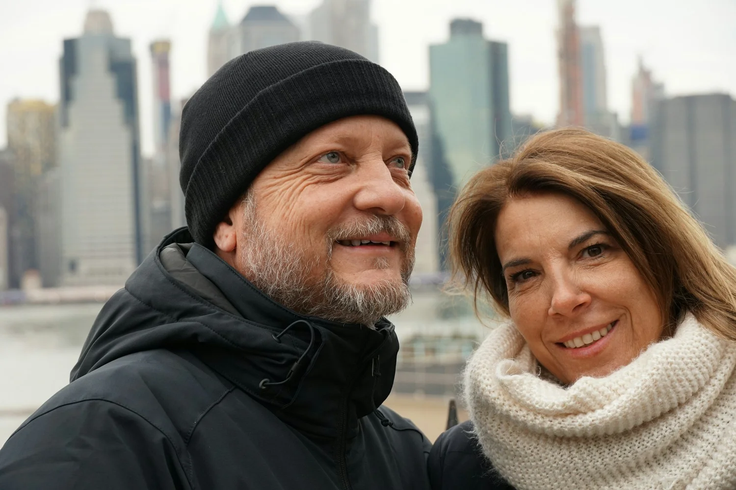 A couple in their sixties outdoors in winter coats, looking off into the distance