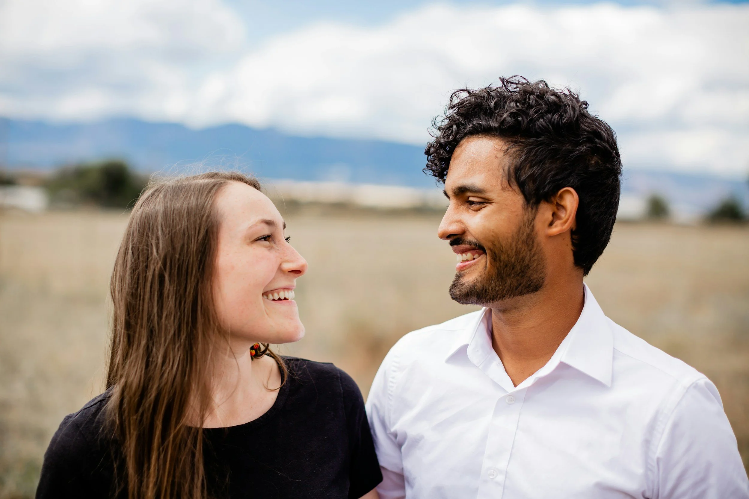 A couple laughing together, facing each other, in a field
