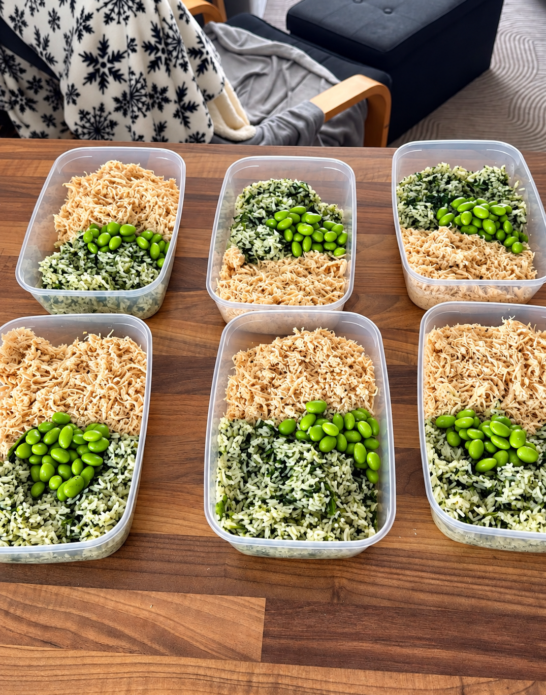 Meal prep containers filled with shredded chicken, chopped cucumber, and green olives on a wooden table.