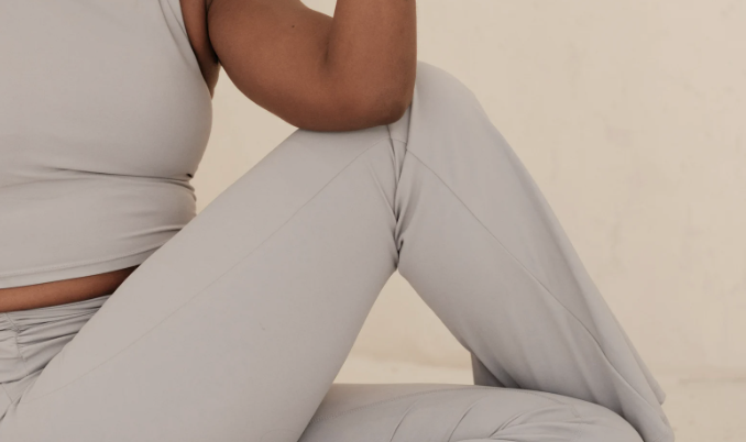Close-up of a person sitting cross-legged on the floor, wearing light-colored workout clothes.