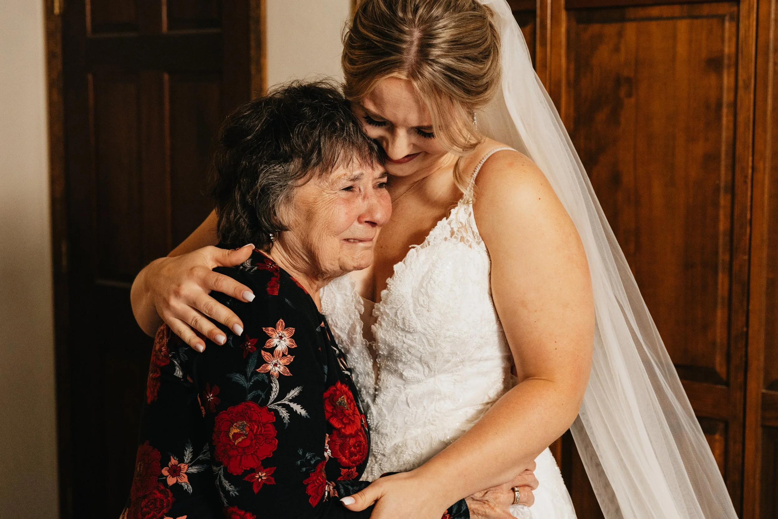 Missoula wedding photographer capturing a bride hugging her grandmother with emotional expressions in a Montana wedding, in front of wooden furniture.