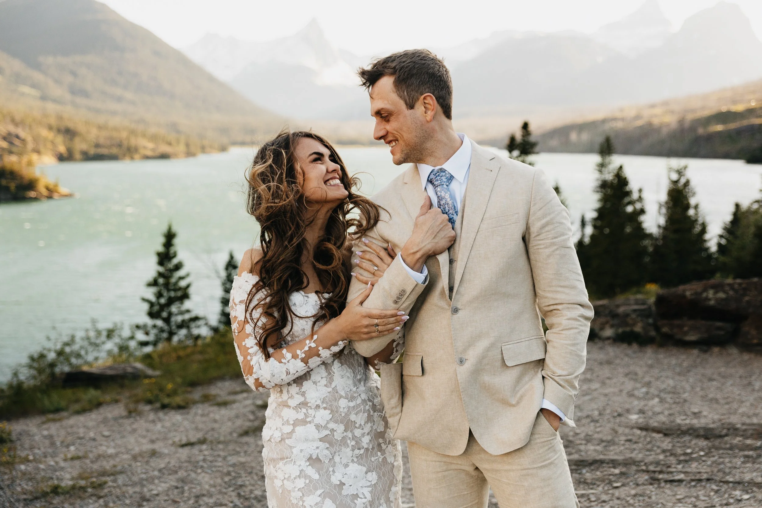 Glacier National Park wedding by a Montana photographer: bride and groom standing outdoors near a lake with forested mountain scenery, celebrating their special day.