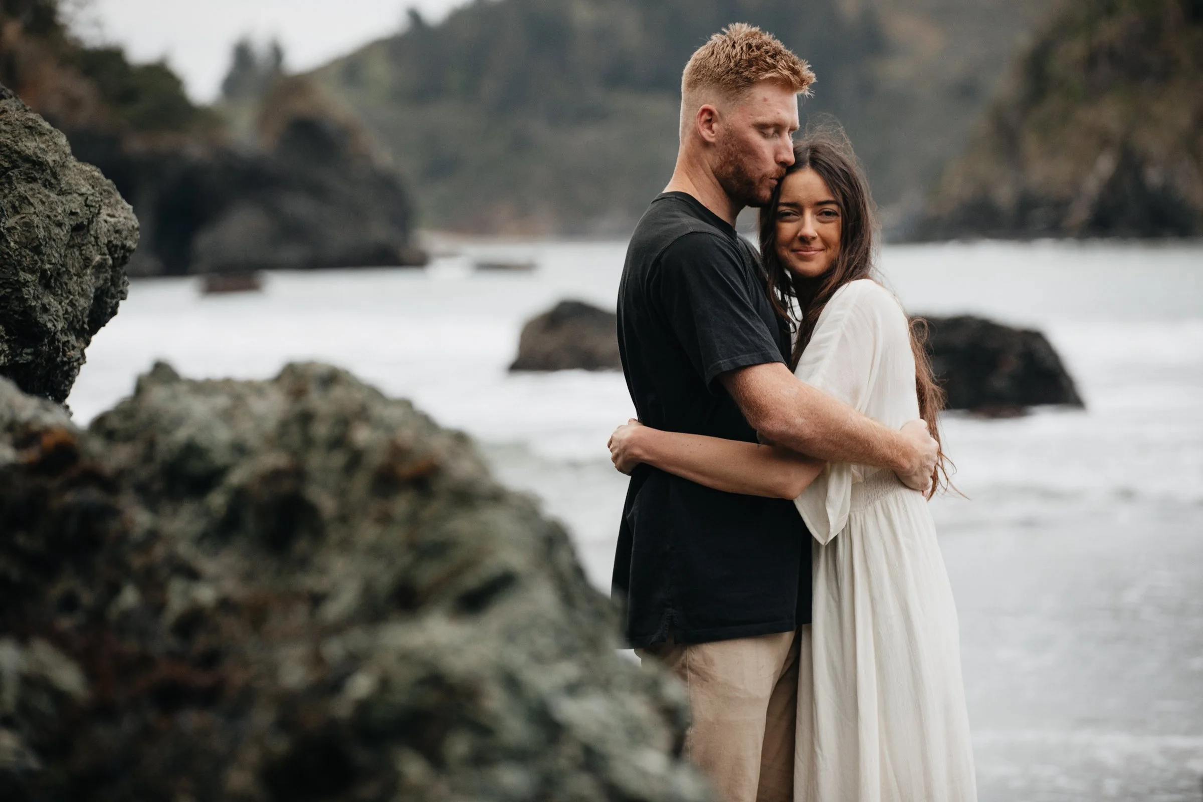 Oregon Coast engagement session with a couple laughing and walking barefoot on the beach at sunset.