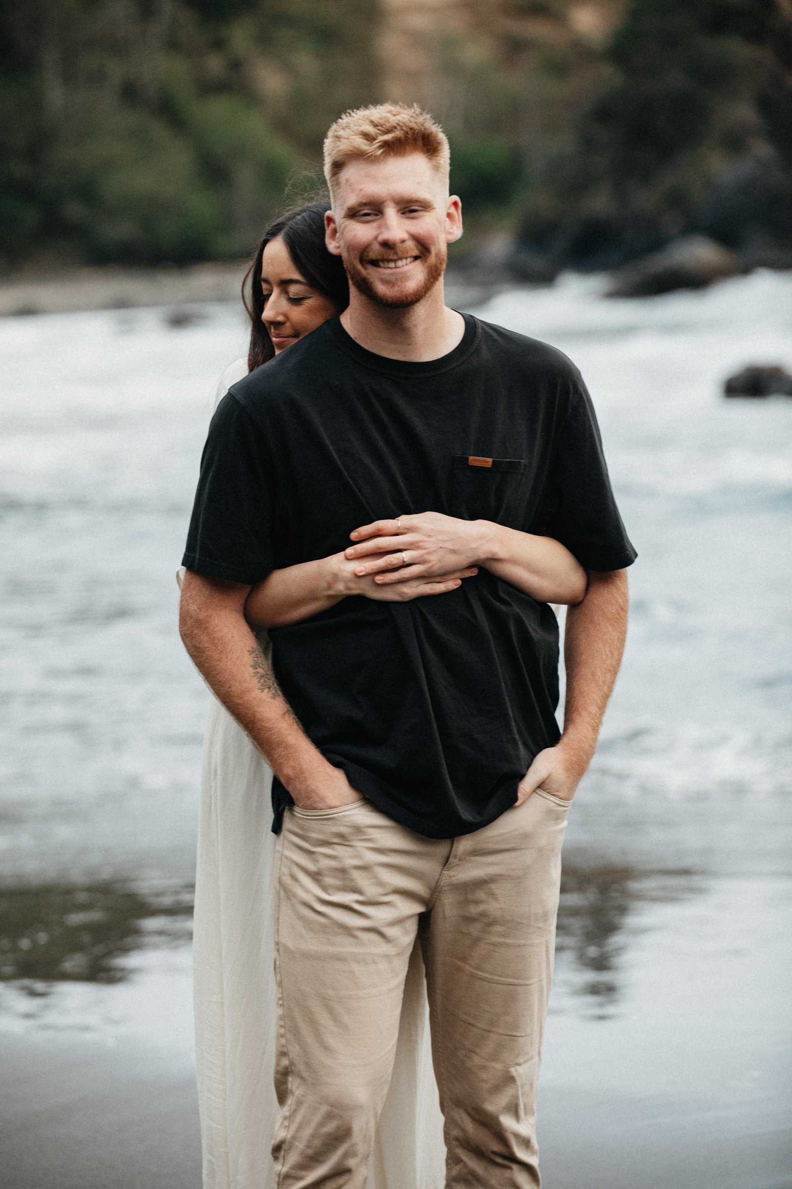 Couple walking along the Oregon Coast beach during an engagement session with dramatic cliffs, ocean waves, and natural coastal light.