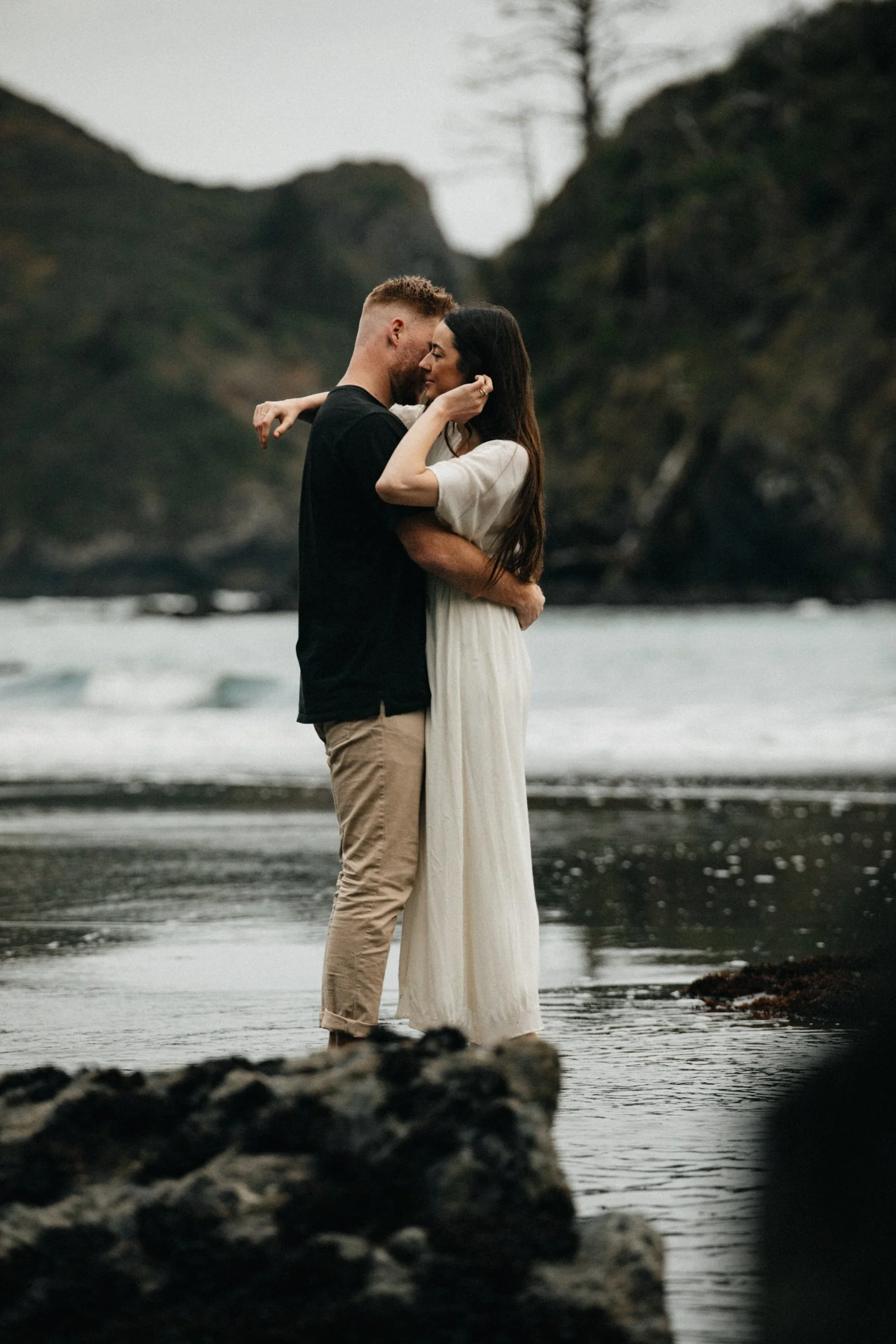 Romantic engagement photos on the Oregon Coast featuring a couple embracing on a sandy beach with moody skies and ocean views.