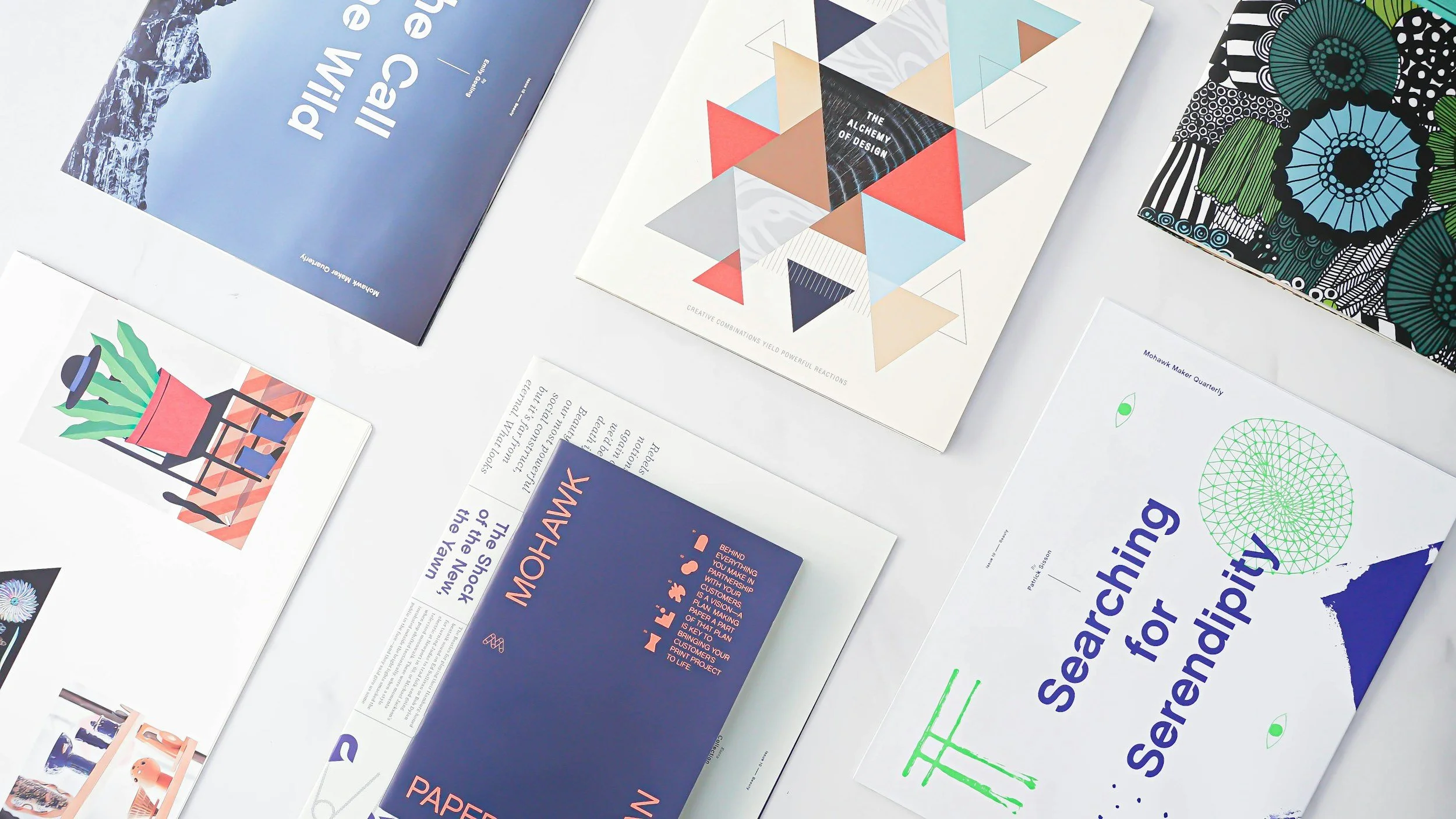 A variety of printed publications and flyers laid out on a white surface, featuring colorful graphics, designs, and text about design, sustainability, and innovation.
