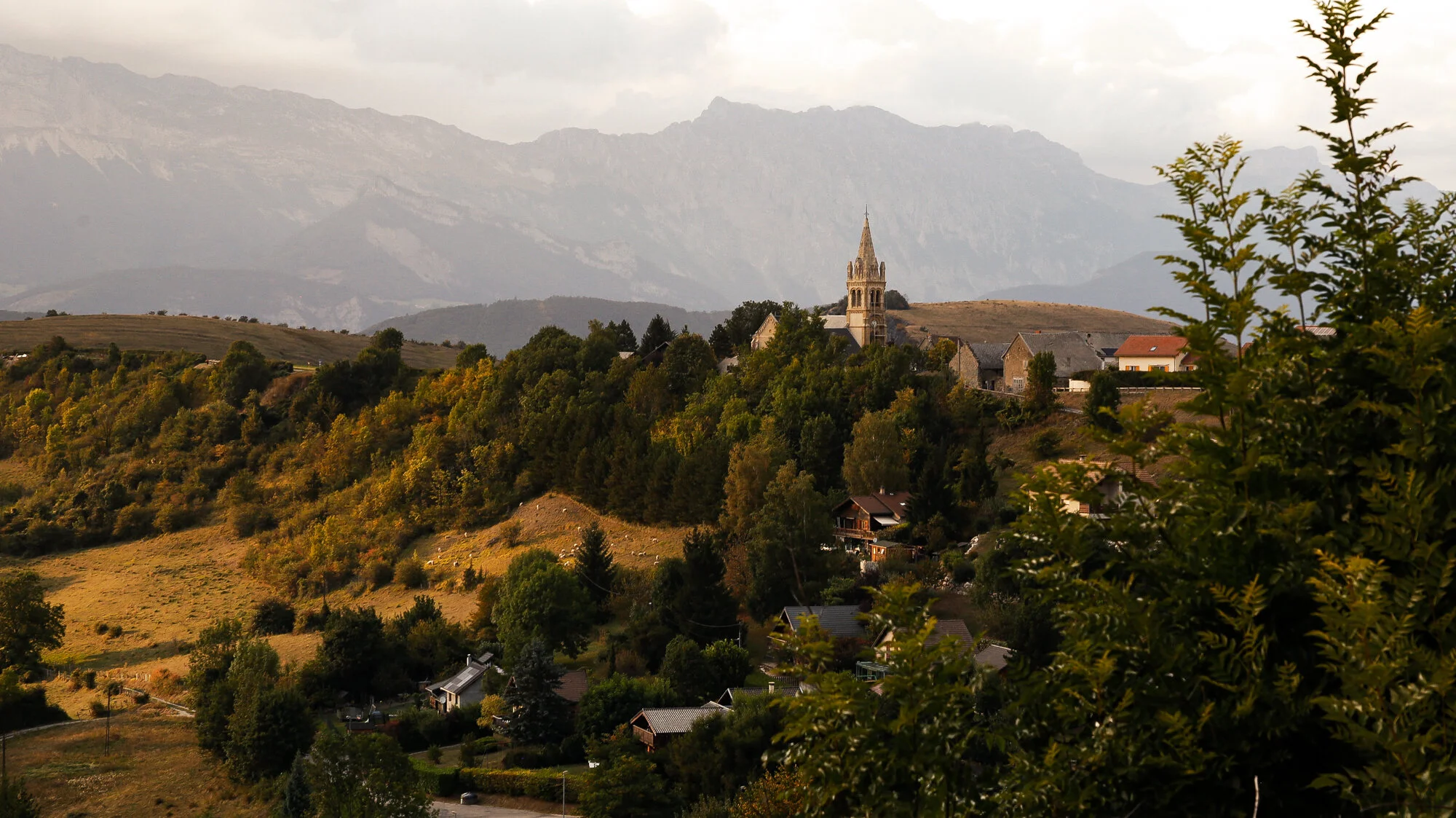 Photo print of a church in the picturesque French village of Monteynard, Auvergne-Rhône-Alpes, with the French Alps in the backdrop at sunset