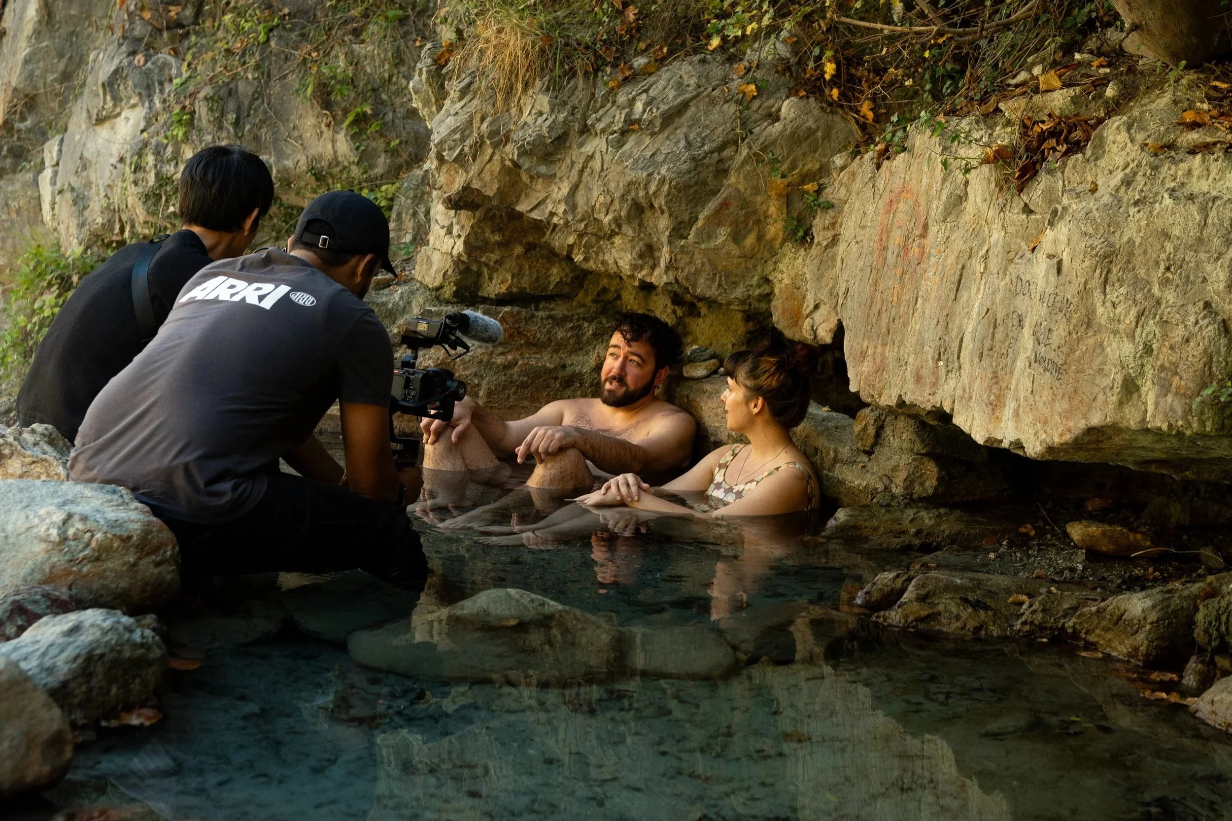 Documentary filmmakers filming in a remote alpine hot spring in the Swiss Alps, capturing geothermal bathing culture during an expedition-based film project