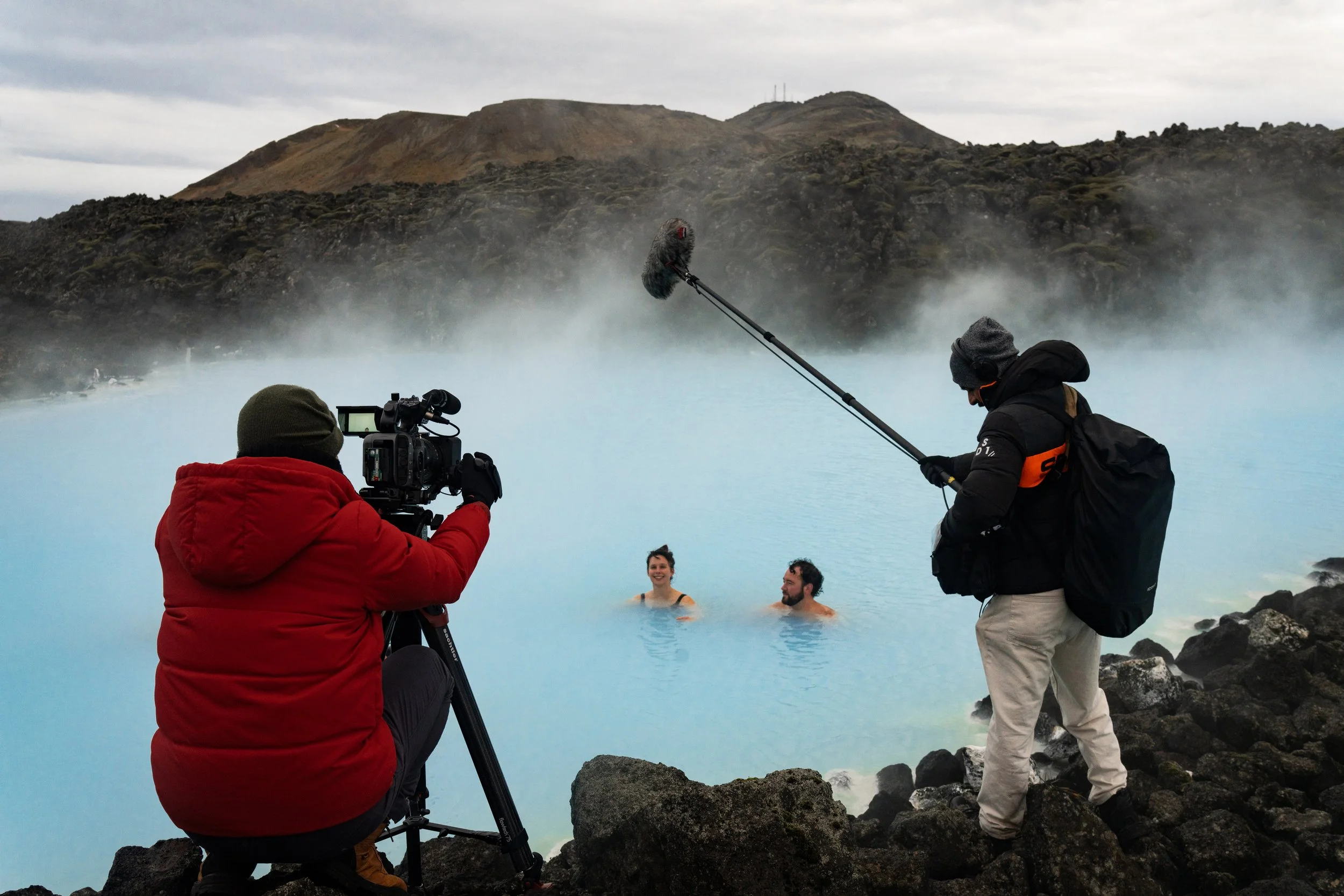 Lucy and Ben filming a documentary scene in the Blue Lagoon, Iceland, with camera and sound crew during a geothermal travel and hot spring filmmaking project