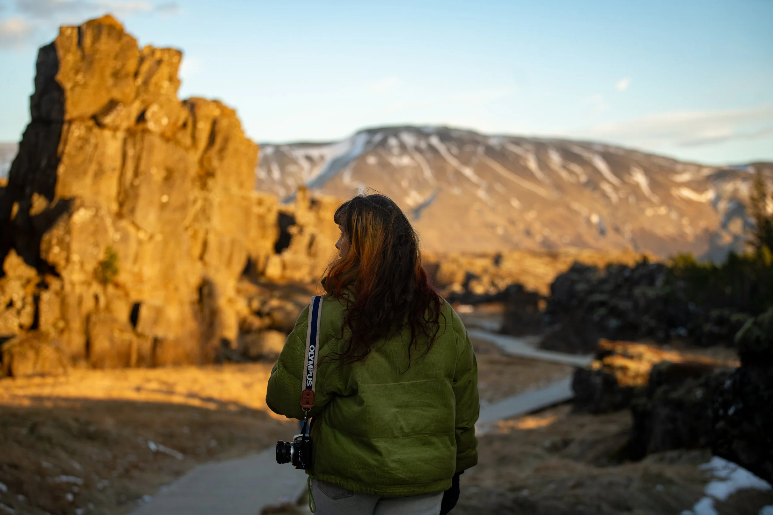 Documentary travel photographer Lucy walking through Þingvellir National Park in Iceland at sunset with an Olympus camera, capturing remote landscapes on a slow travel journey