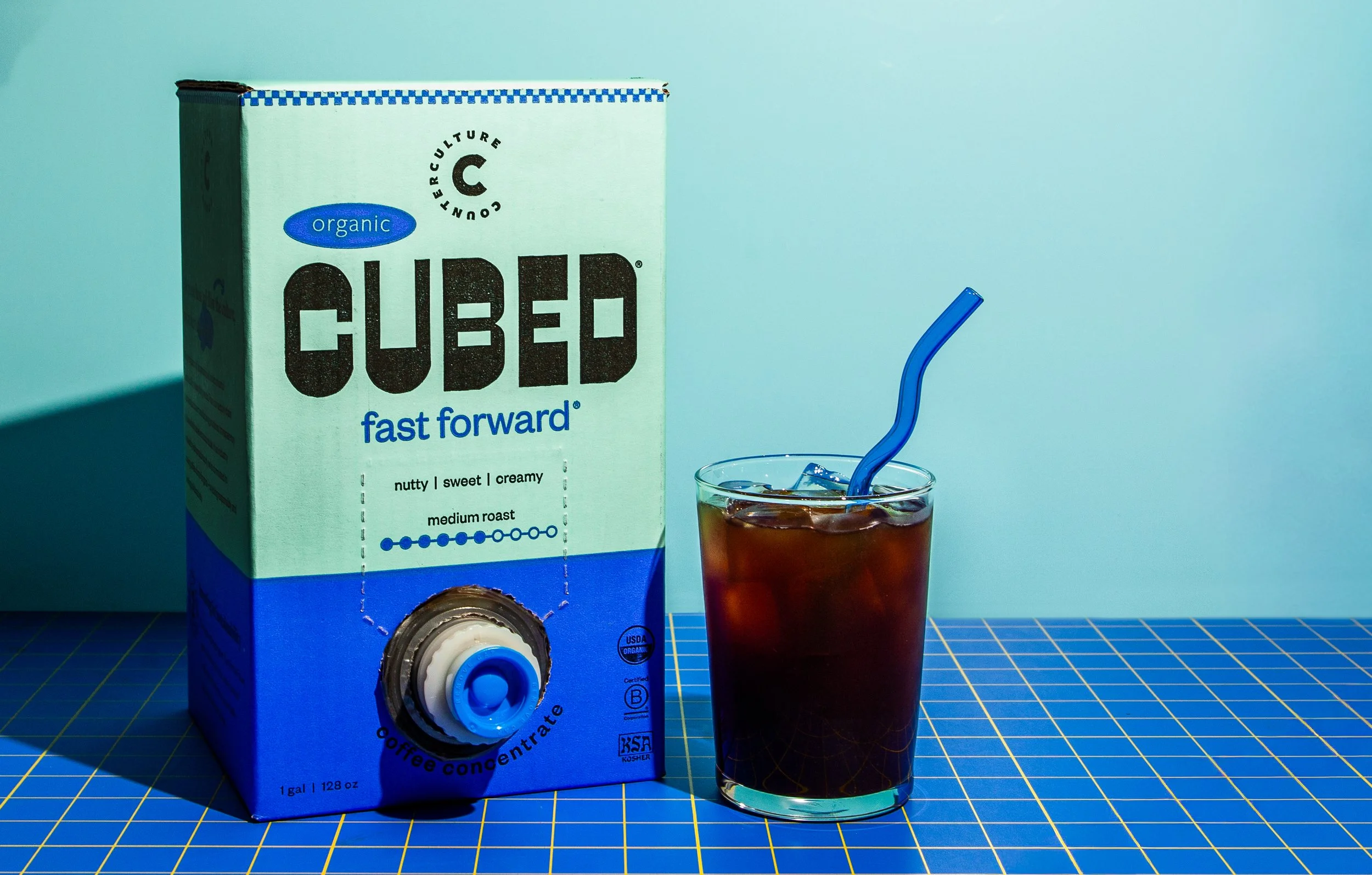 Cubed Counter Culture Coffee organic concentrate packaging — mint and blue bag in box with fast forward blend and iced coffee glass on blue grid surface