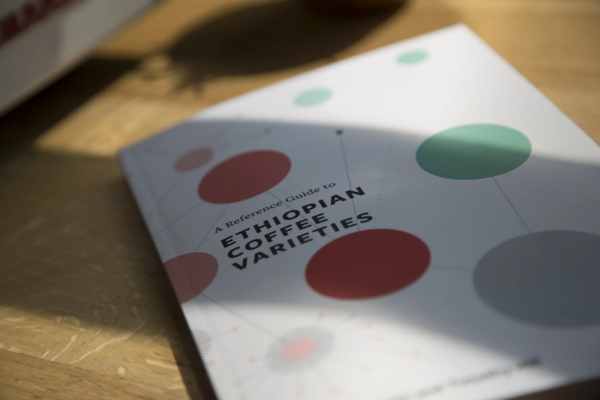 A Reference Guide to Ethiopian Coffee Varieties book cover — white cover with colorful circle pattern on wooden surface
