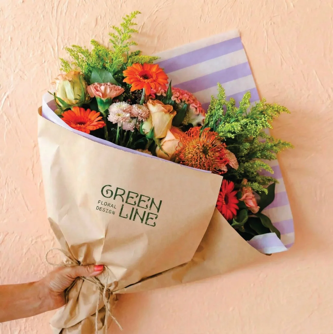 Green Line Floral Design branded kraft paper bouquet wrap — logo printed on flower packaging held against peach wall