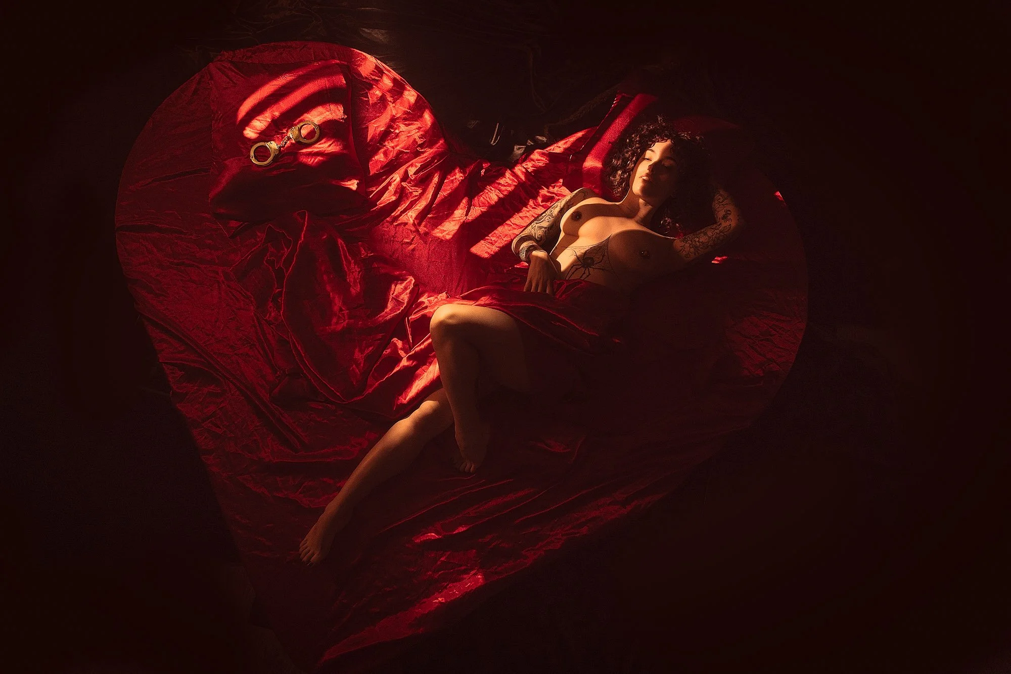 Framed like a movie poster, this intimate photo features woman laying on a heart shaped bed covered with red sheets