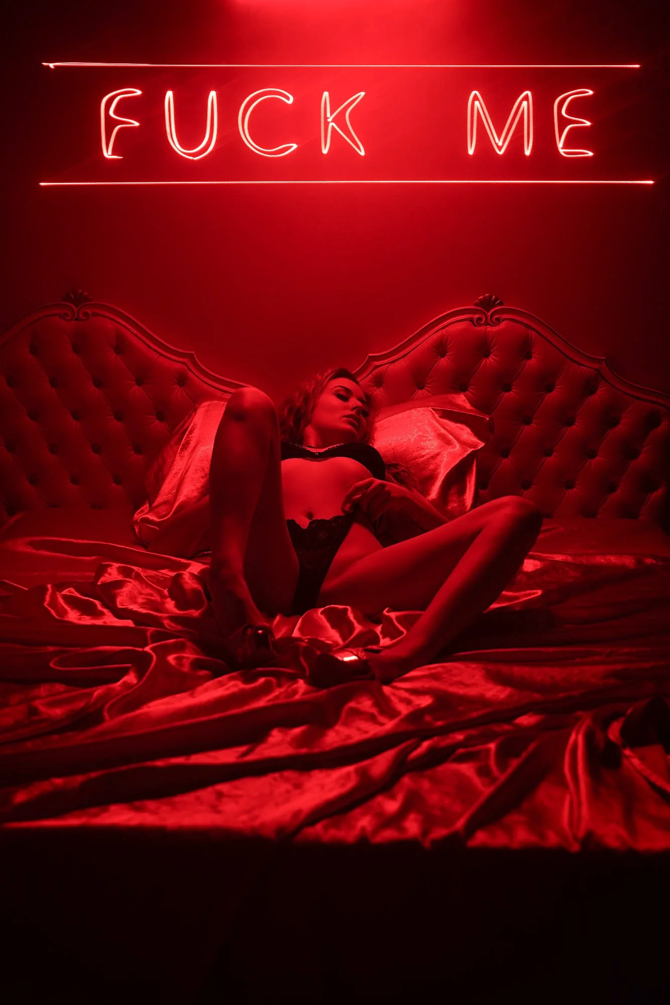 Movie poster-like photo featuring woman arching on a bed in a red light with a hot neon sign above her.