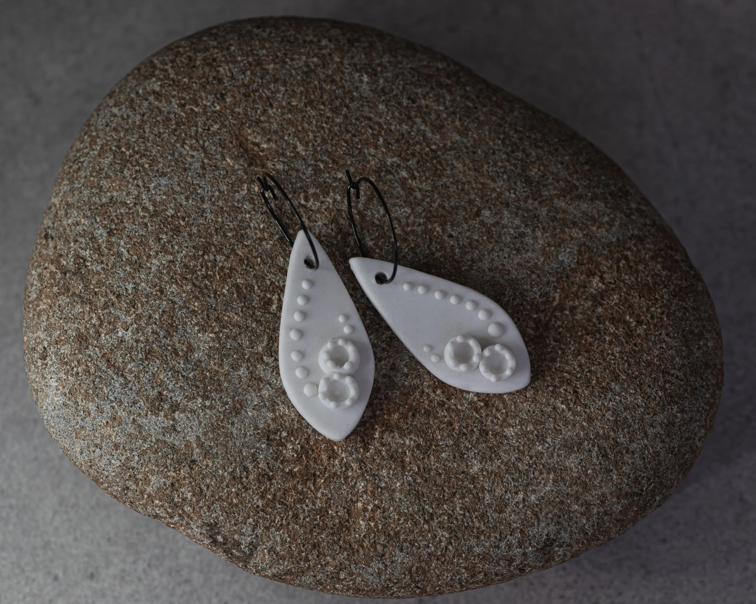 PELLA porcelain earrings with raised slip dots and lichen cups sitting on a rock.