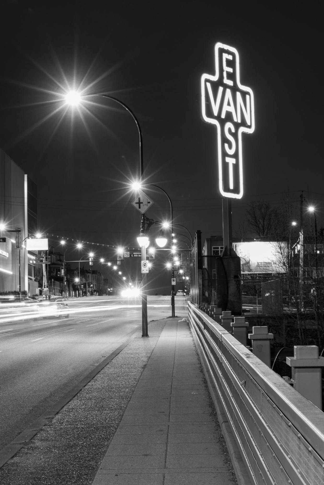 Nighttime street scene in Vancouver with a lit neon sign reading 'VAN ST' and streetlights illuminating the sidewalk and road.