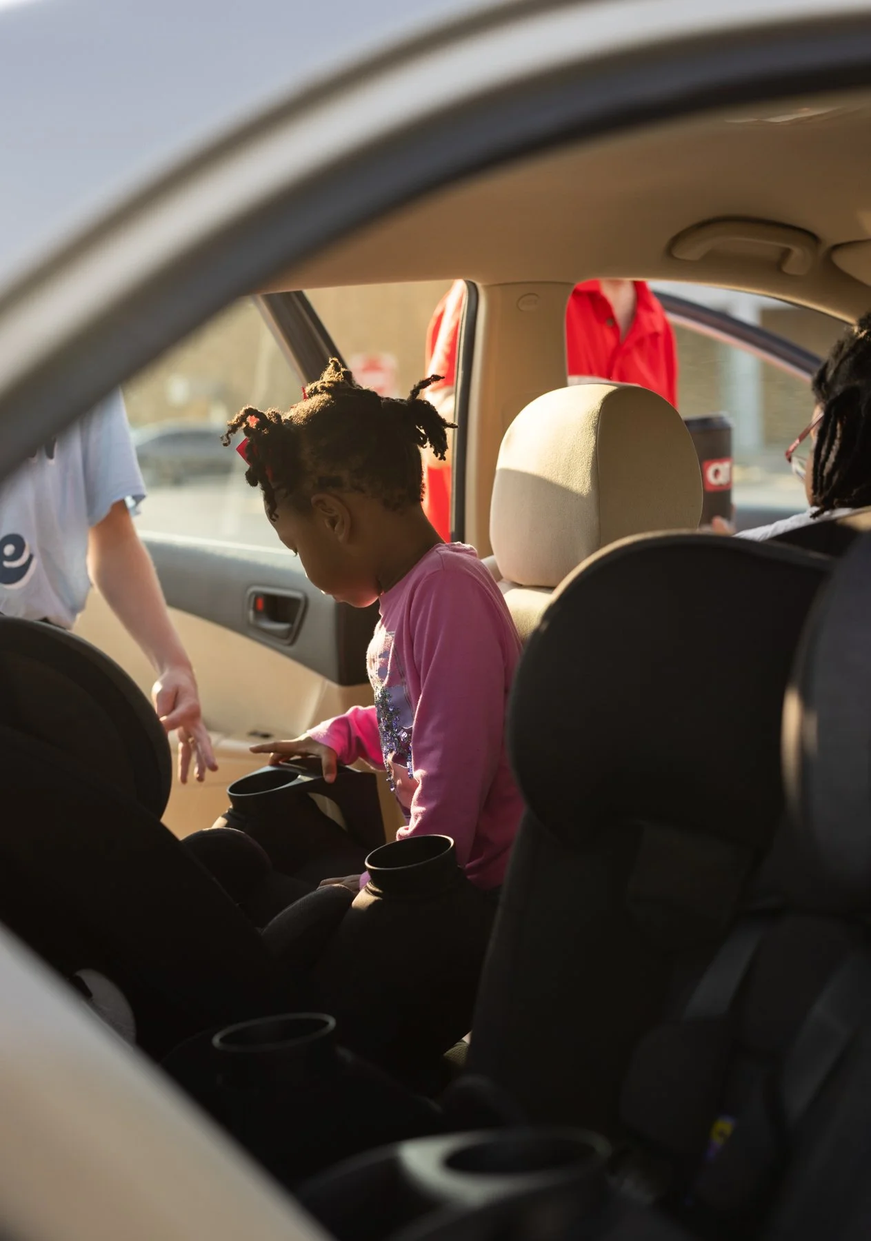 Child putting something in a car seat inside a donated vehicle, with a person outside the car reaching in, and two adults standing nearby.