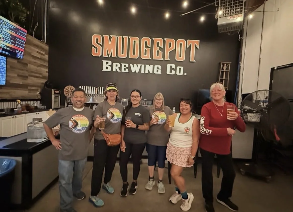 A group of six people standing inside a bar called Smudgepot Brewing Co., holding drinks and smiling for the photo.
