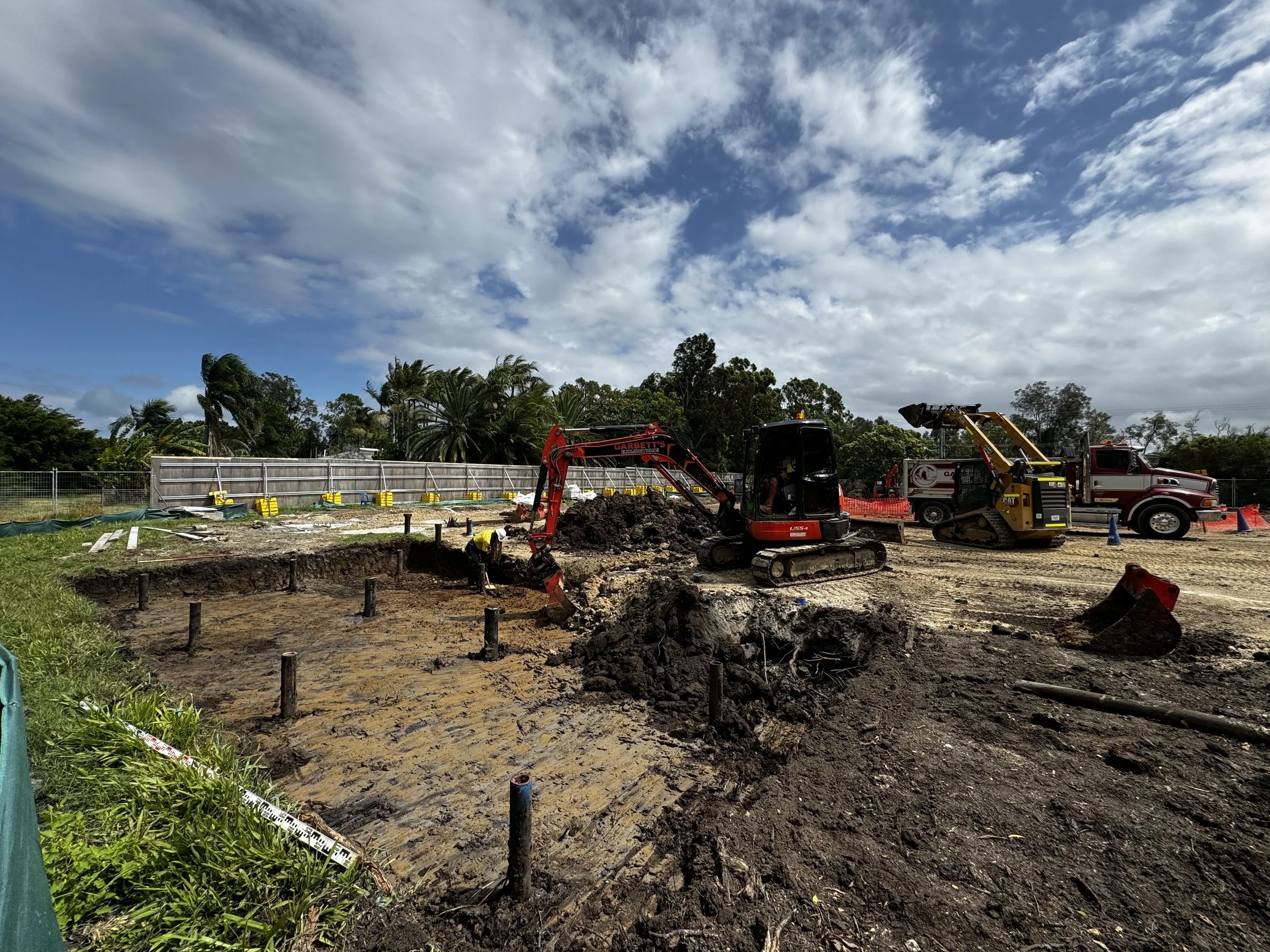 A synchronised effort unfolds as multiple machines, including excavators and tipper trucks, coordinate screw pile digs and transport materials off-site for the Northern Rivers Schools upgrade project, in partnership with ADCO Constructions. Garbett's