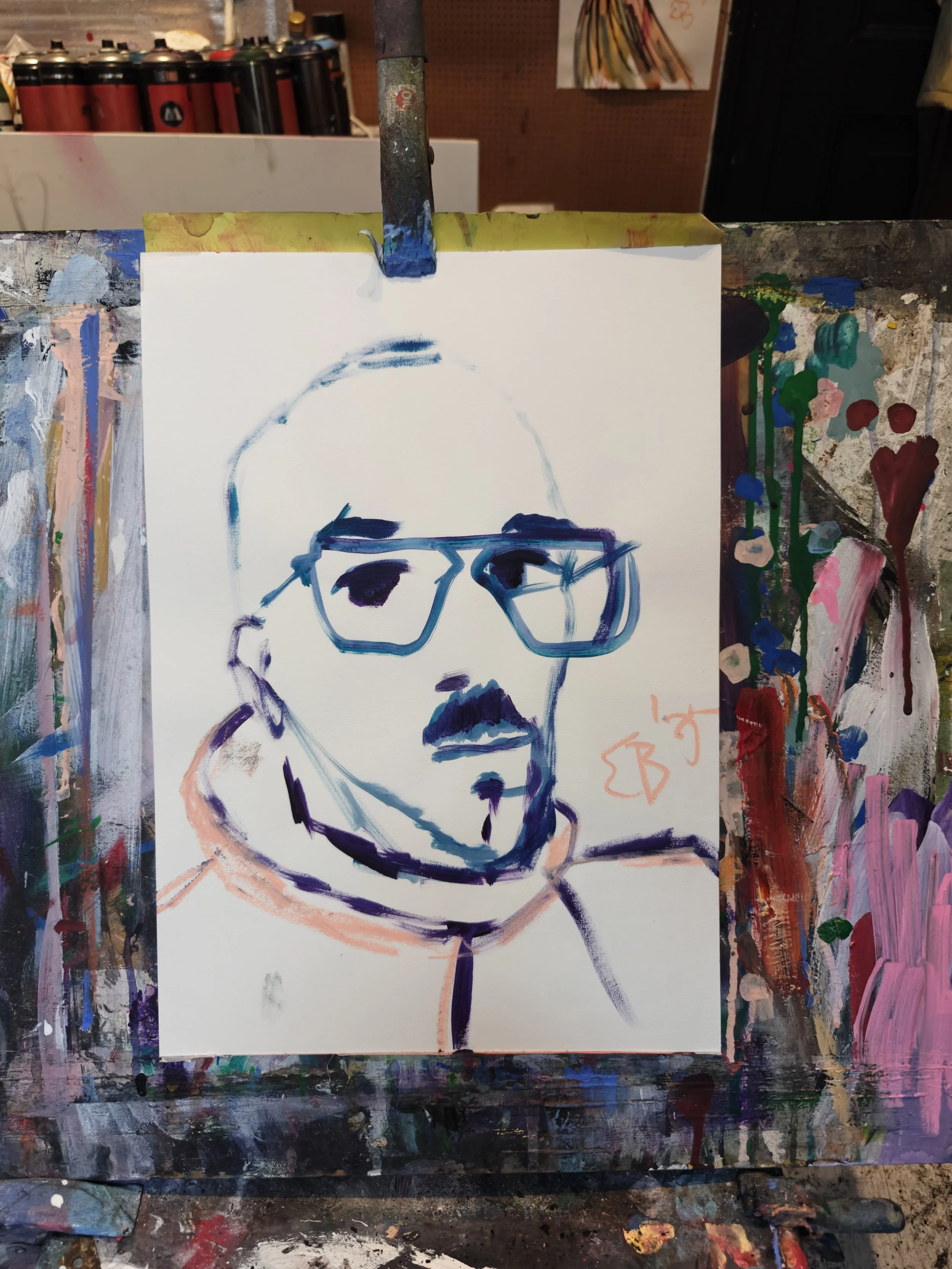 A colorful, abstract portrait of a person with glasses, short hair, and a mustache, painted on a white canvas with visible brushstrokes, surrounded by a paint-splattered easel.