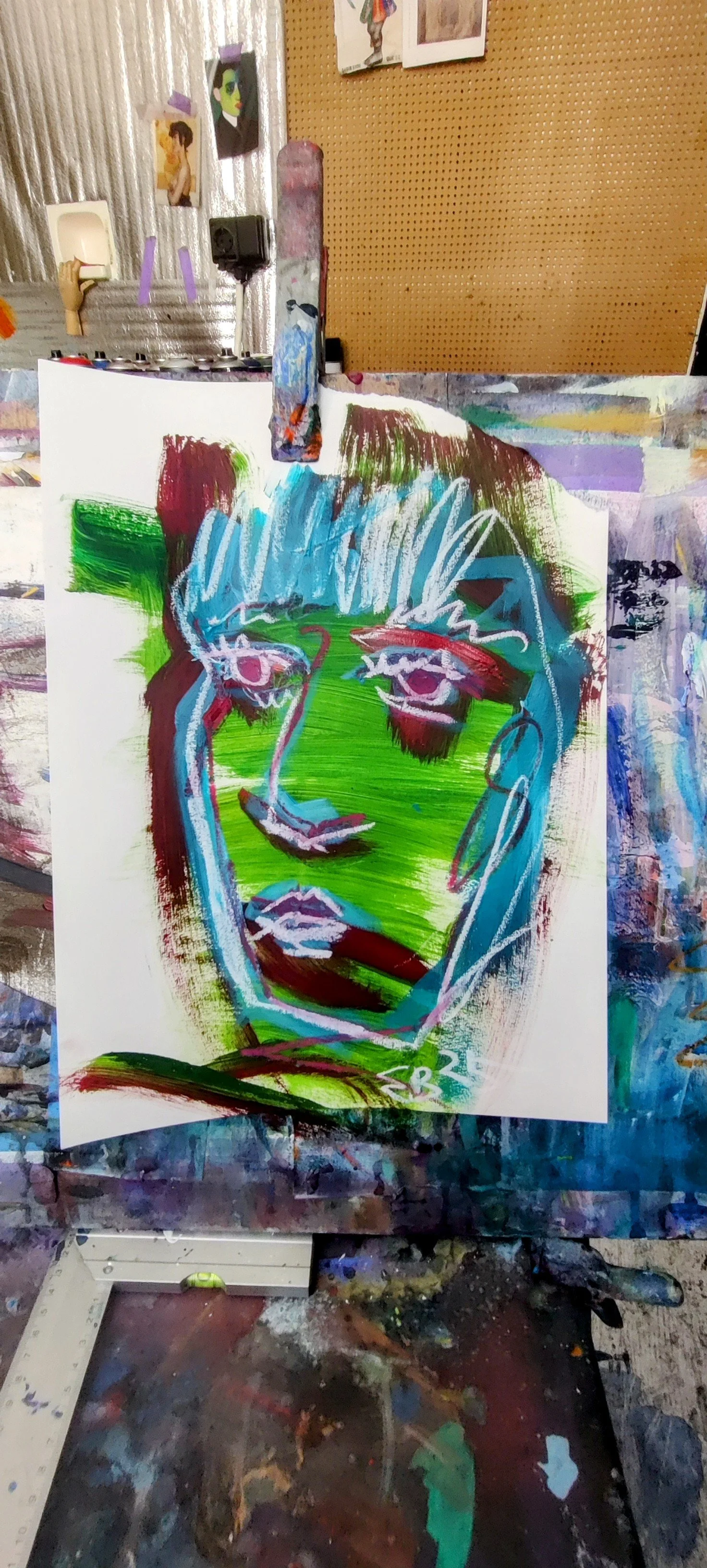 Colorful abstract portrait of a face with prominent eyes, nose, and lips, painted with bold brushstrokes in shades of green, blue, red, and purple on a white canvas.