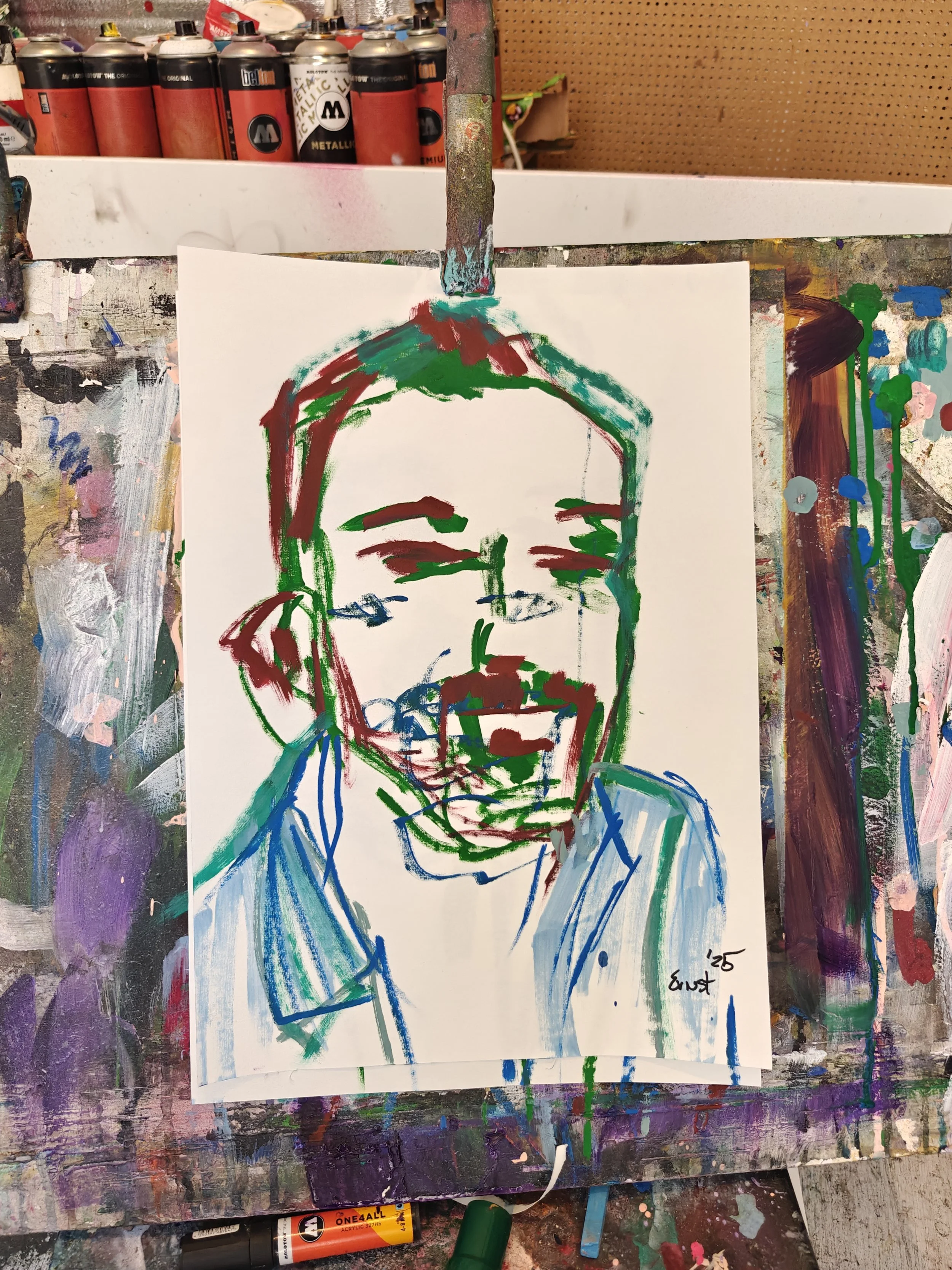 Abstract colorful painting of a person laughing, using bold lines and vibrant colors, on a cluttered art workspace with spray paint cans in the background.