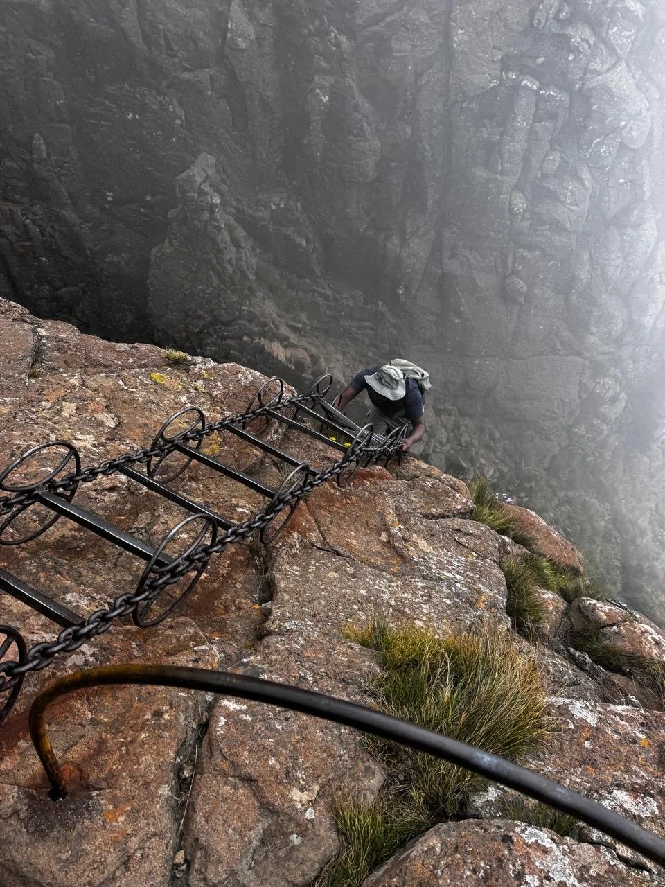 Someone ascending the chain ladders to the top of the Tugela Waterfalls, the highest waterfall in the world. The steel chain ladders are anchored onto the cliff face and are suspended down the rock for about 35m. Moderate hike with a thrilling ascent