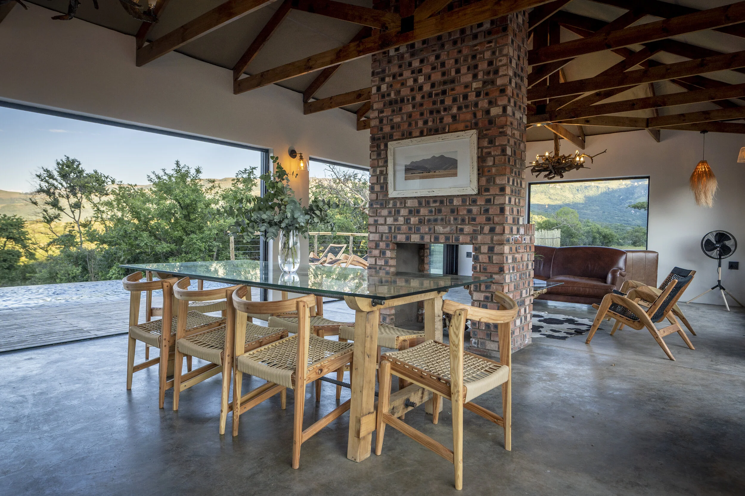 A beautifully styled African minimalist dining space, with open stack doors dissolving the boundaries between indoors and the natural world beyond. Clean lines, natural textures and understated elegance create a serene setting where the landscape bec